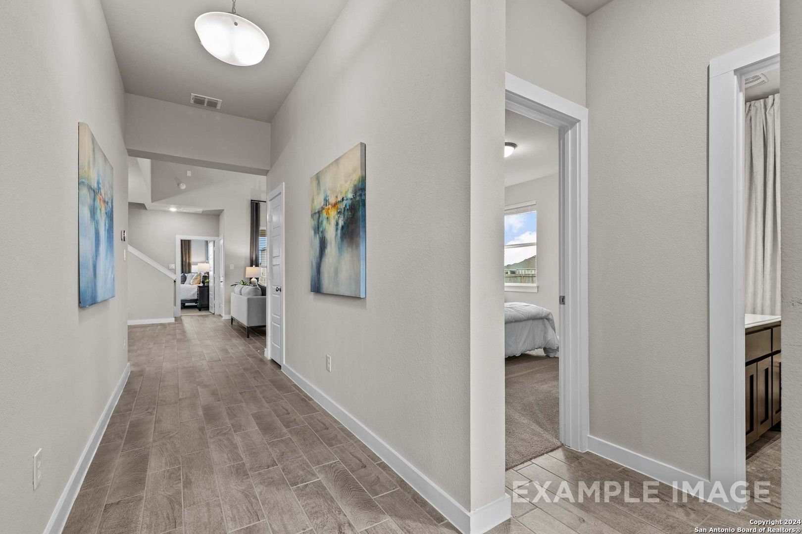 Elegant hallway with hardwood floors and abstract art leading to bright bedroom and bathroom in The Collin B, Seguin, Texas