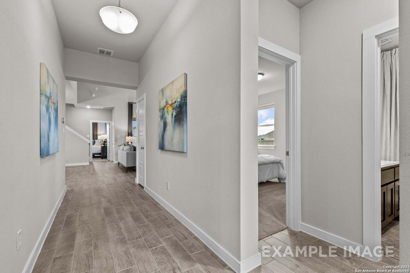 Elegant hallway with light wood floors, abstract wall art, leading to bedroom and bathroom in The Collin A floor plan, Seguin, Texas
