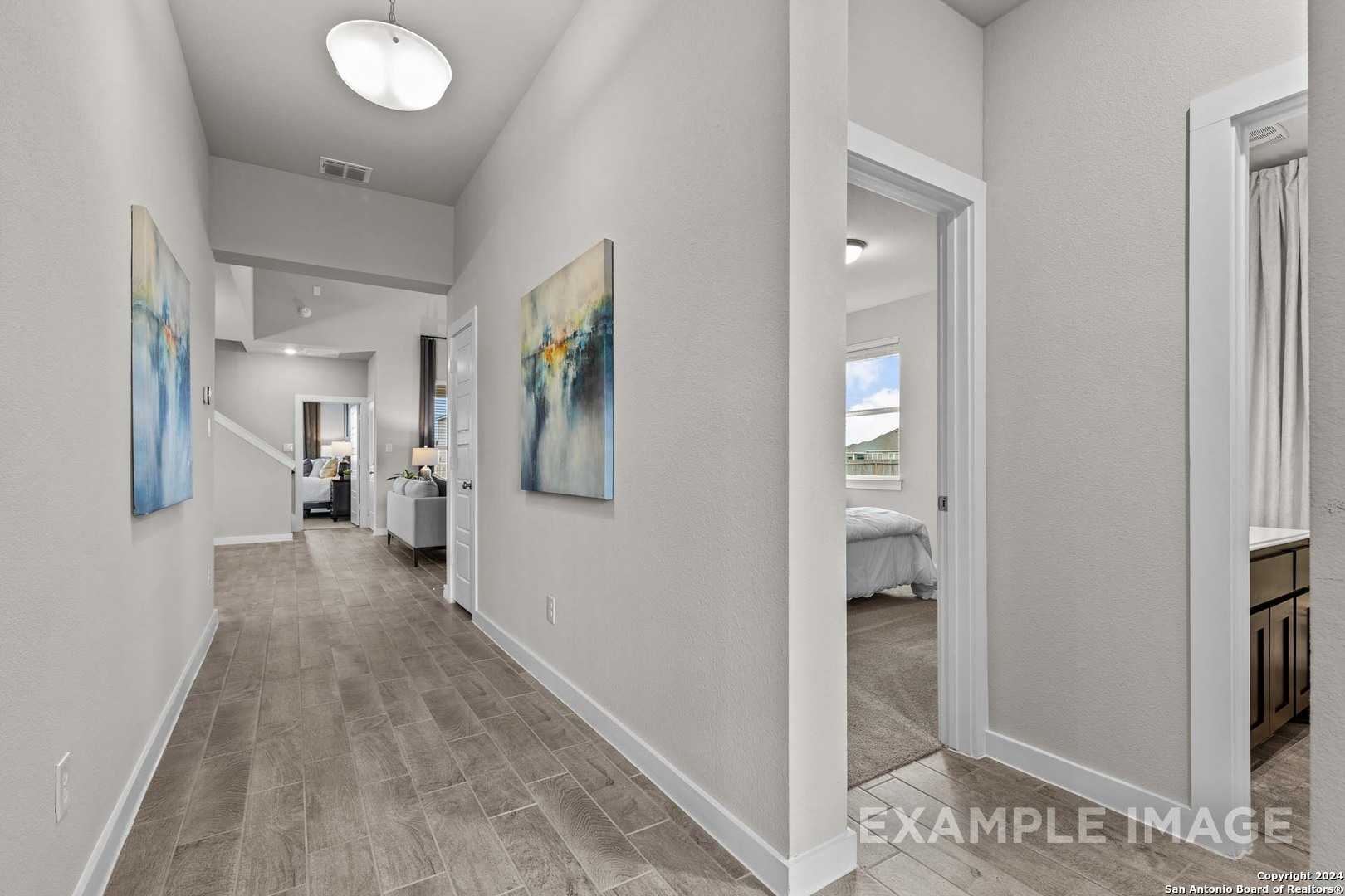 Elegant hallway with hardwood floors and abstract art leading to bright bedroom and bathroom in The Collin B, Seguin, Texas
