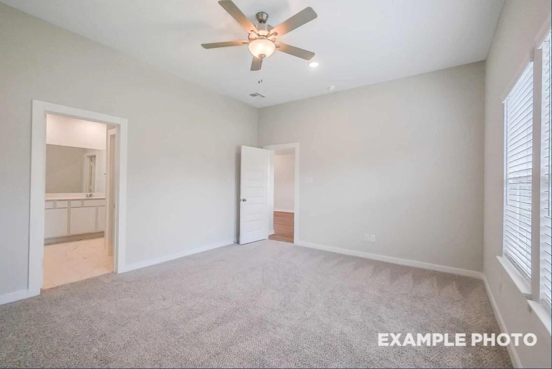 Carpeted secondary bedroom with ceiling fan, window blinds, and open bathroom door featuring vanity in Davidson Homes The Riviera C, Dayton, Texas
