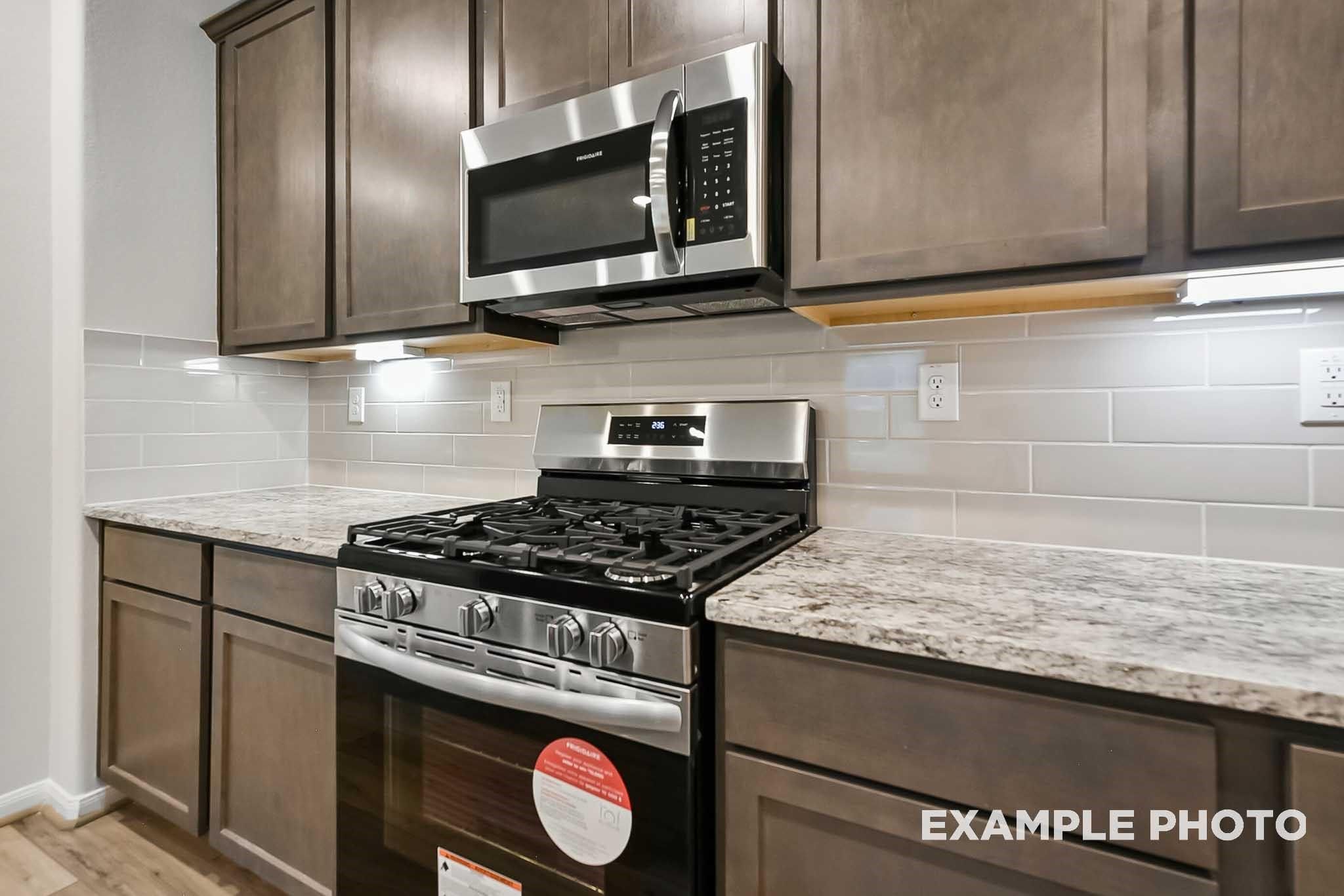 Modern kitchen with granite countertops, stainless steel gas range, and subway tile backsplash in The Blanco F, Conroe, TX.
