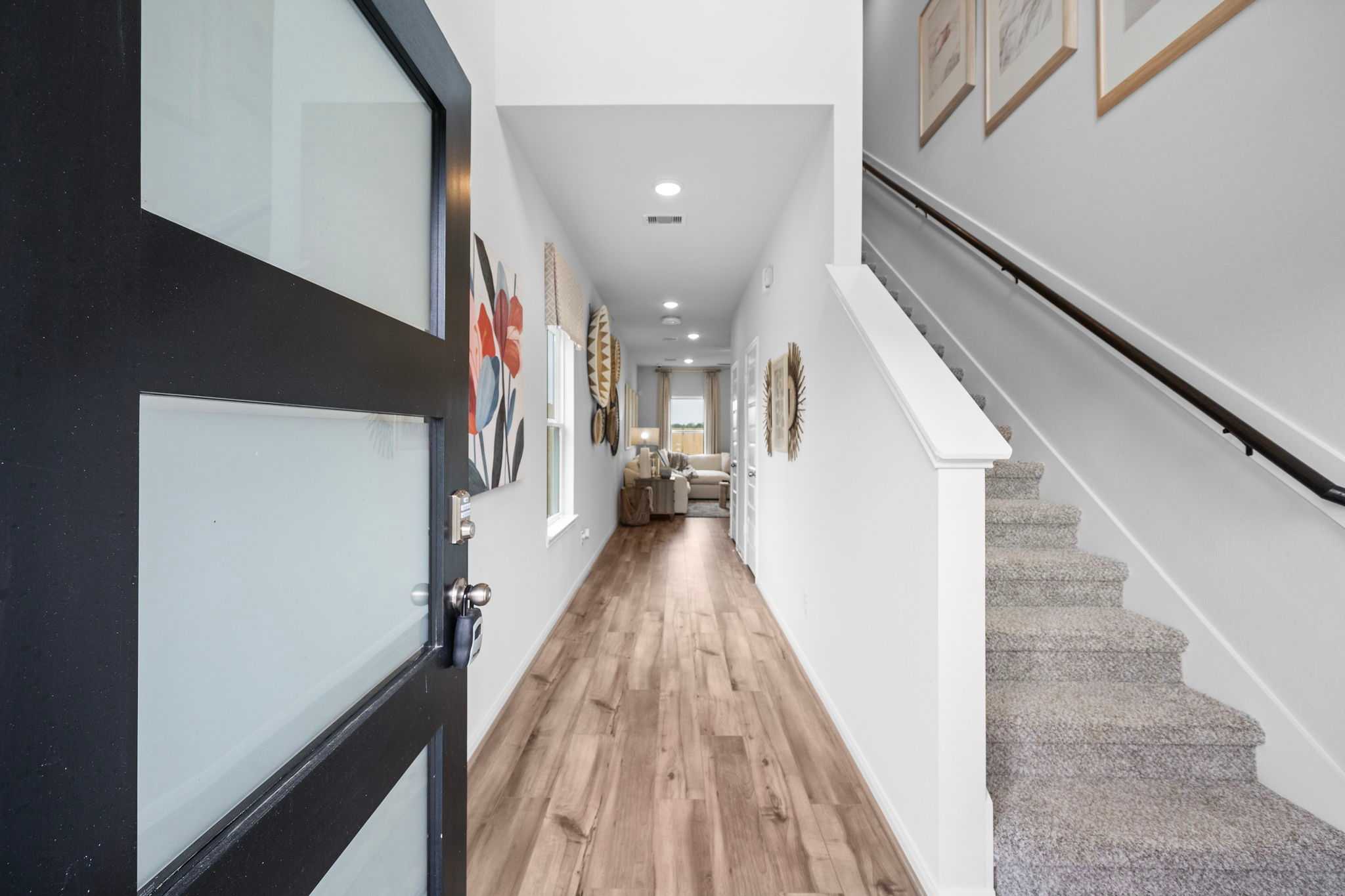 Spacious entry hallway at Spring Branch Crossing in Conroe TX with hardwood floors, carpeted staircase, and modern wall art