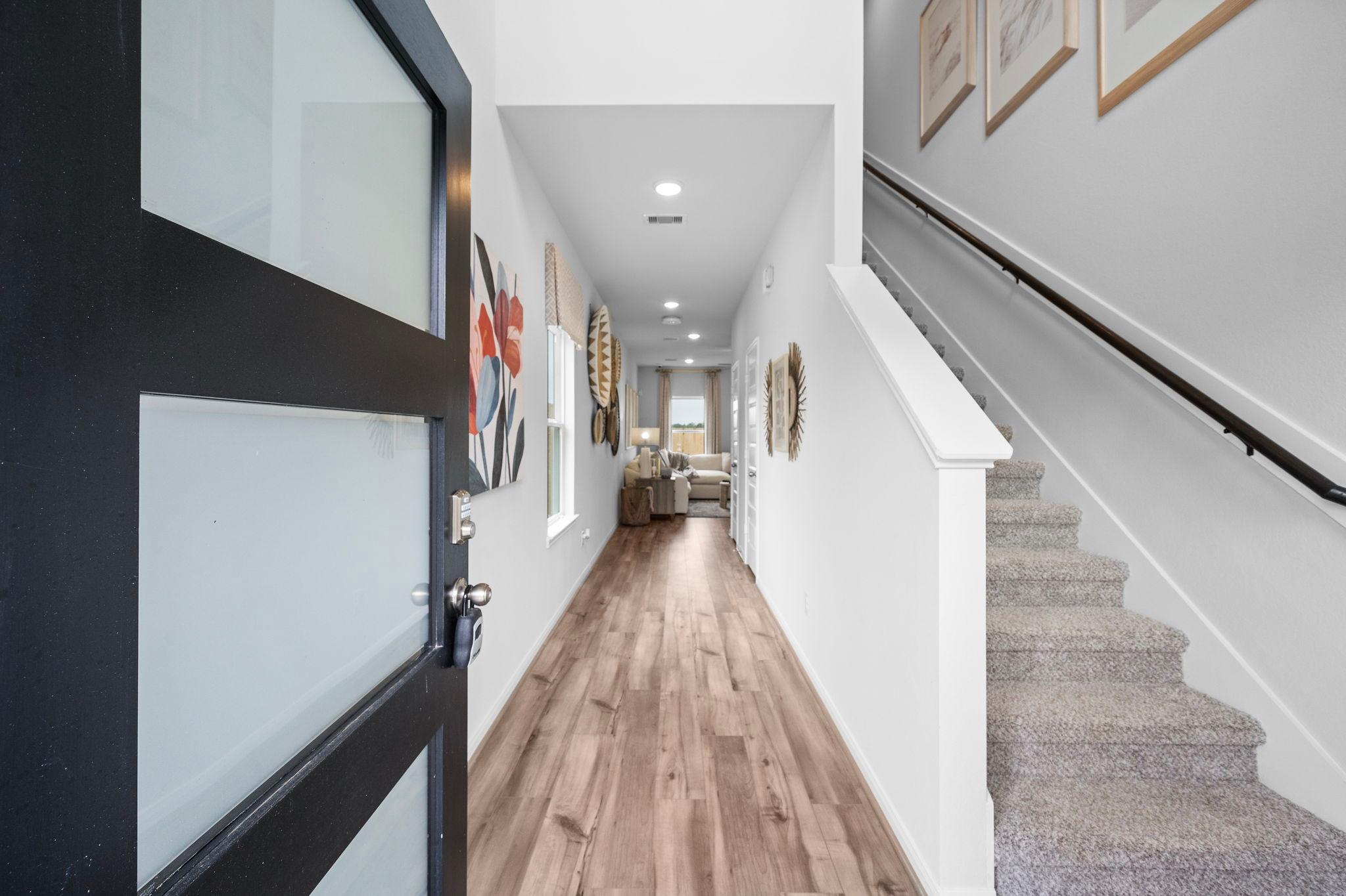 Spacious entry hallway at Hill & Dale Ranch in Splendora Texas featuring hardwood floors white walls art and carpeted staircase