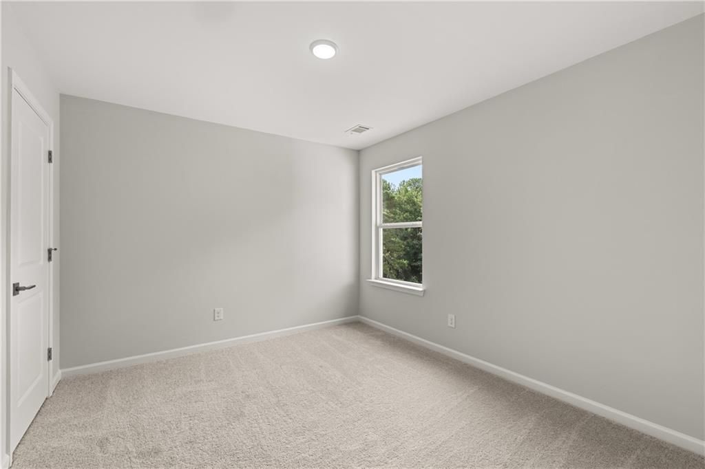 Bright, carpeted secondary bedroom with neutral walls in The Russell A floor plan at Cedar Farms in Winder, Georgia.