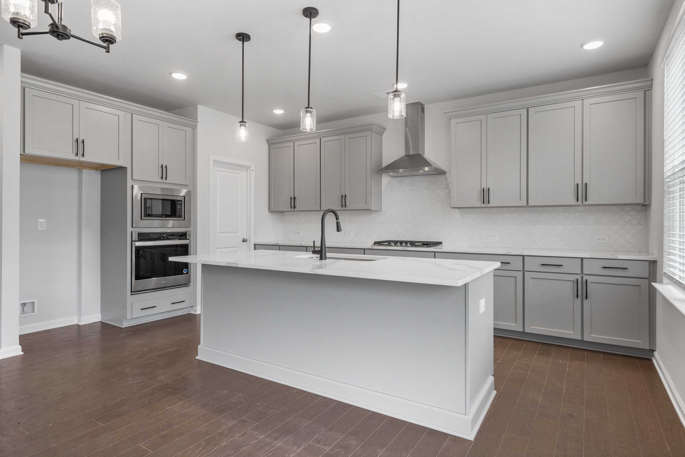 Contemporary kitchen at Reverie at East Lake in McDonough GA with light gray cabinets, white island, pendant lights, hardwood floors