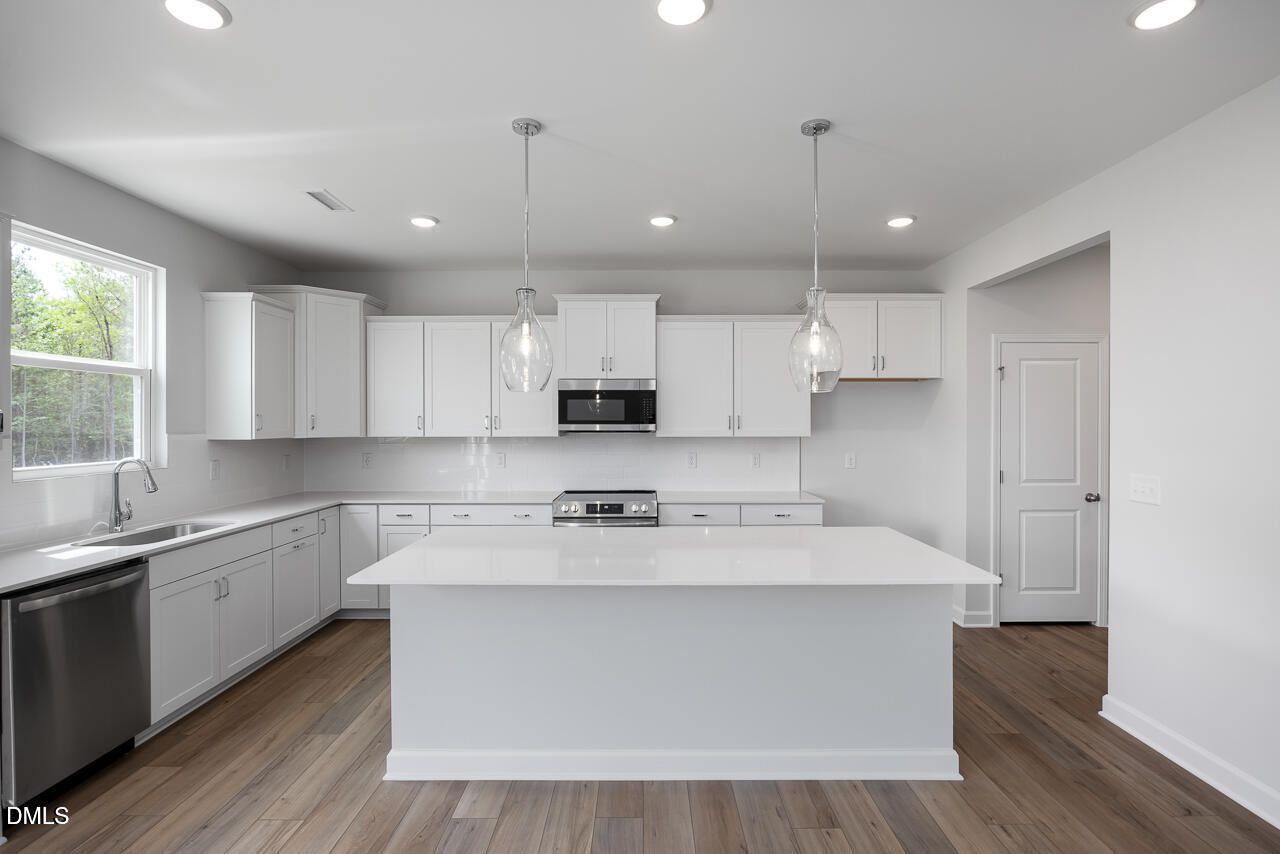 Modern white kitchen with large island, stainless steel appliances, and pendant lights in Davidson Homes The Hickory II C, Zebulon, NC