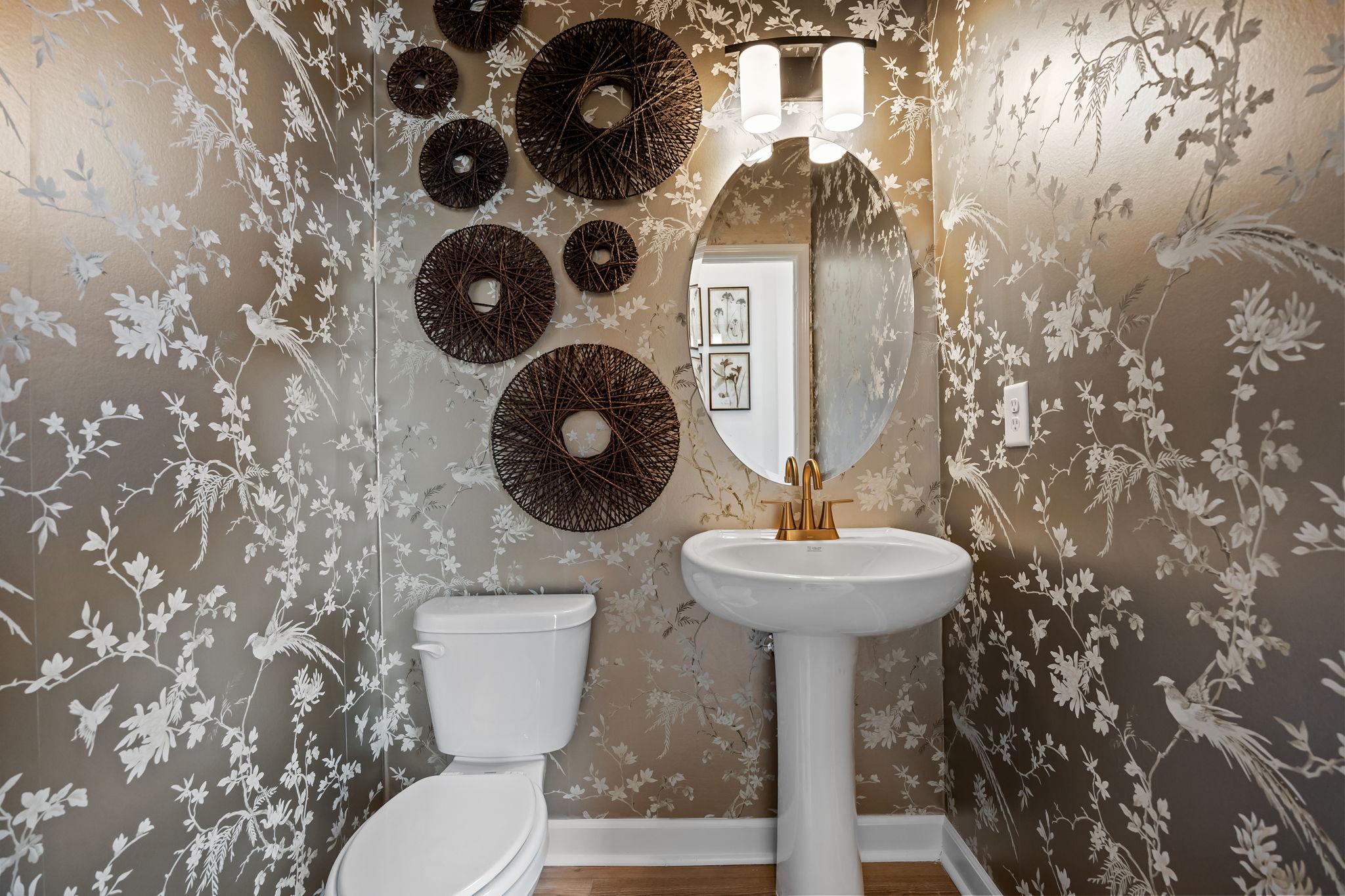 Elegant powder room at Camden Park in Knightdale NC with silver floral wallpaper, woven wall decor and pedestal sink