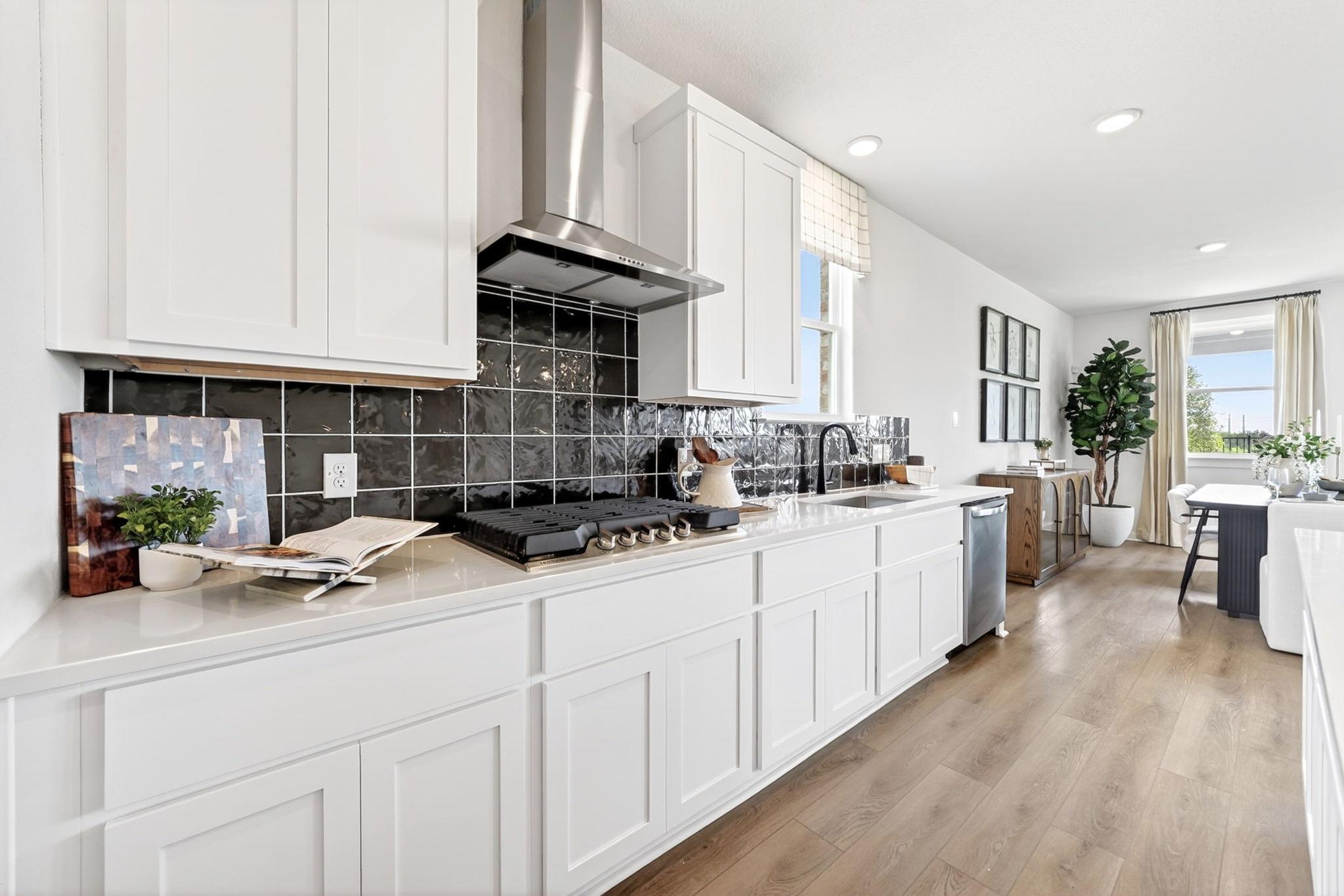 Modern kitchen at Parks at Foster Crossing in Anna, TX with white cabinetry, black tile backsplash, and hardwood floors.