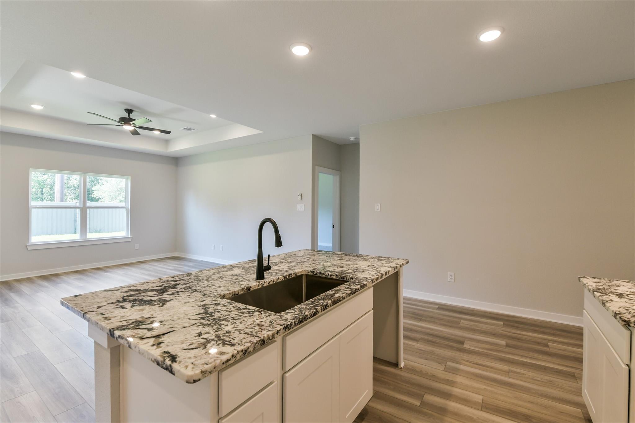 Modern open-concept kitchen with granite island, black faucet sink, white cabinets in The Daphne H by Davidson Homes, Crosby, Texas