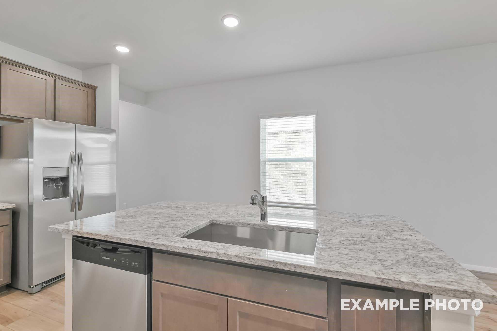Modern kitchen featuring granite island sink, stainless steel fridge and dishwasher in Davidson Homes The Frio F, Conroe, Texas