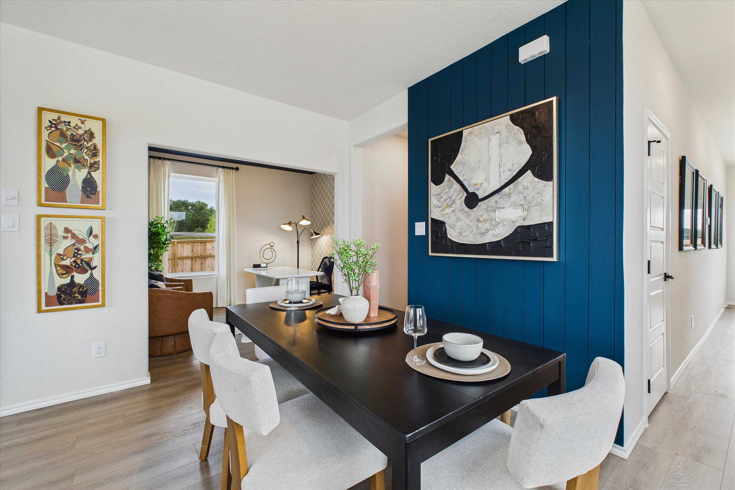Modern dining area with navy accent wall, abstract art, wooden table, and upholstered chairs in Davidson Homes The Florence C, San Antonio
