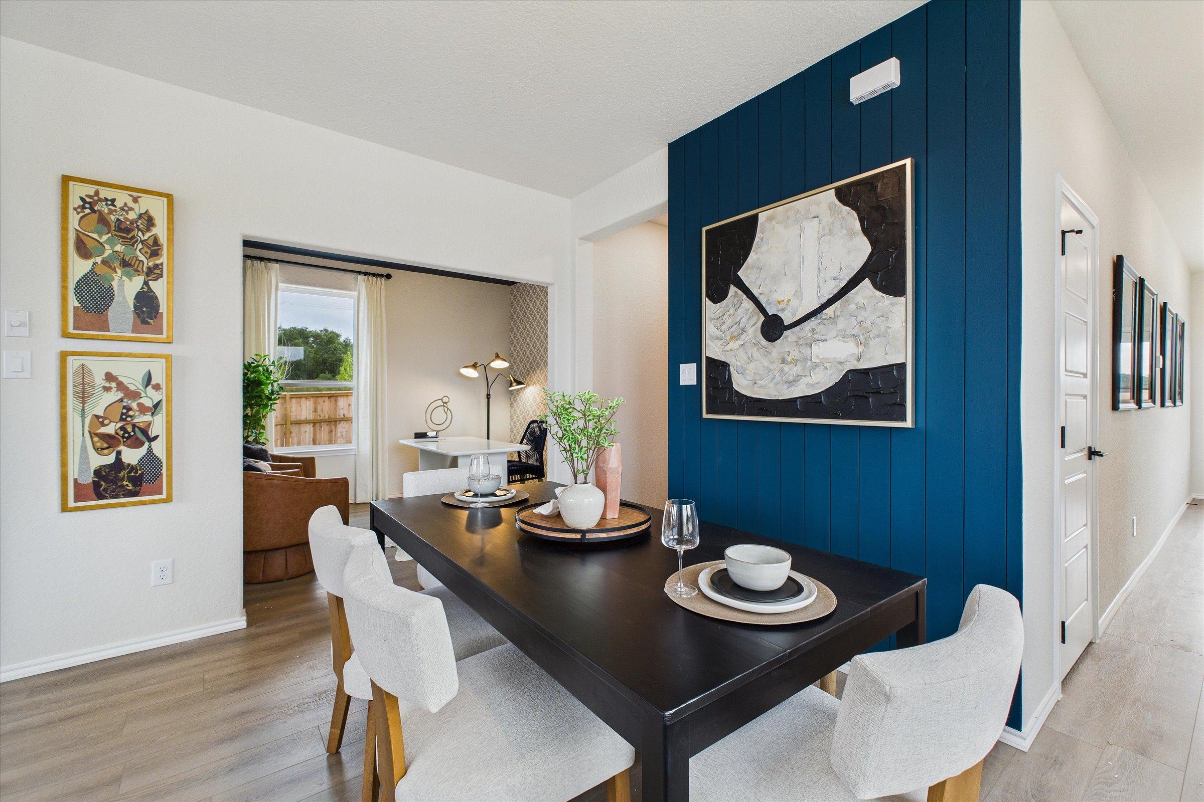 Modern dining area with navy accent wall, abstract art, wooden table, and upholstered chairs in Davidson Homes The Florence C, San Antonio