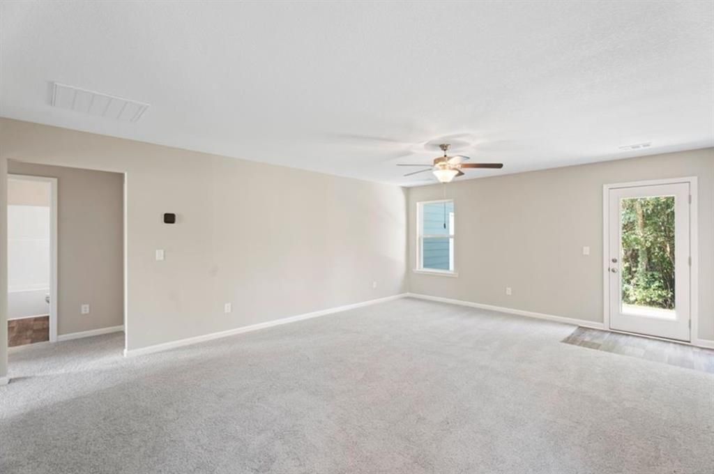 Bright living room with beige walls, ceiling fan, carpeted floor, large window, and glass door to backyard in Davidson Homes The Washington, Phenix City