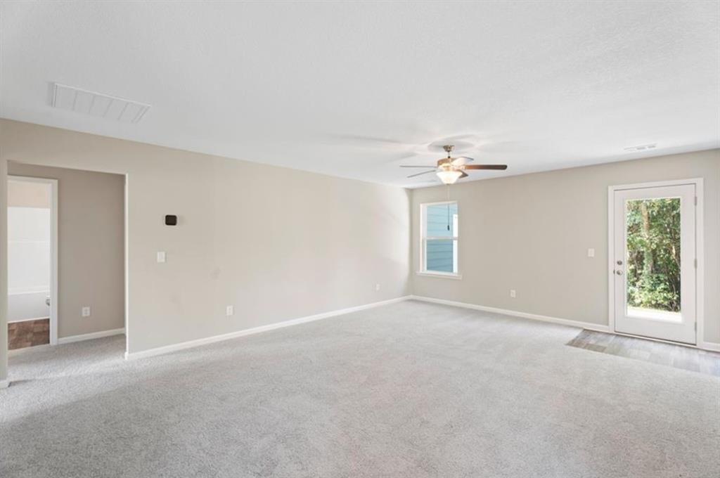 Bright living room with beige walls, ceiling fan, carpeted floor, large window, and glass door to backyard in Davidson Homes The Washington, Phenix City