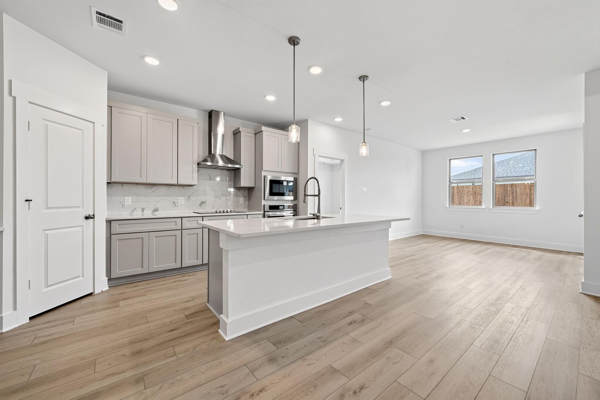 Open-concept kitchen with white island, pendant lights, and wood-look flooring in Davidson Homes Holly F plan, Josephine, TX