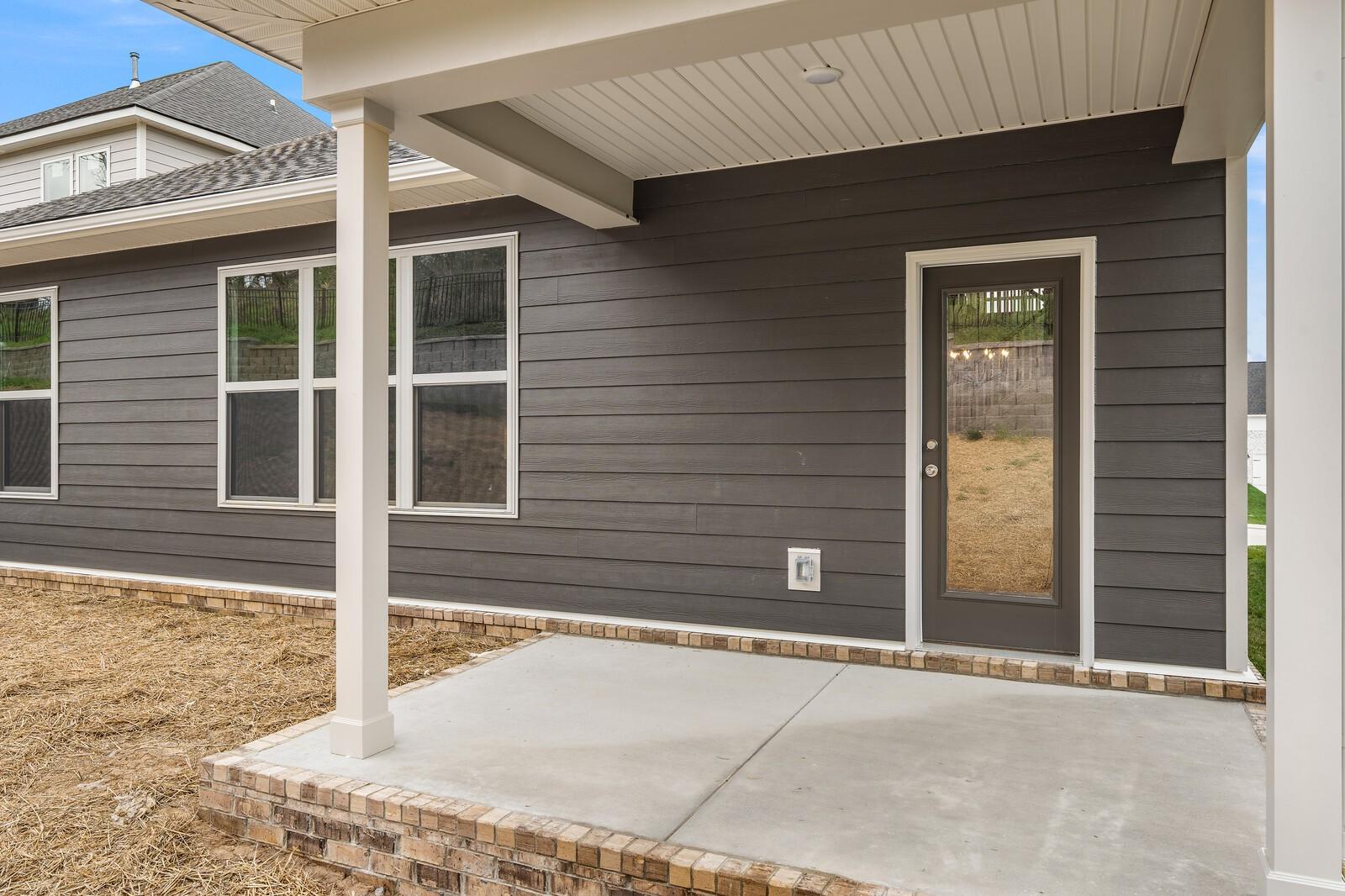 Covered back patio with concrete deck, glass door, and large windows on gray-sided 2-story home in Woods Crossing, Gallatin, Tennessee