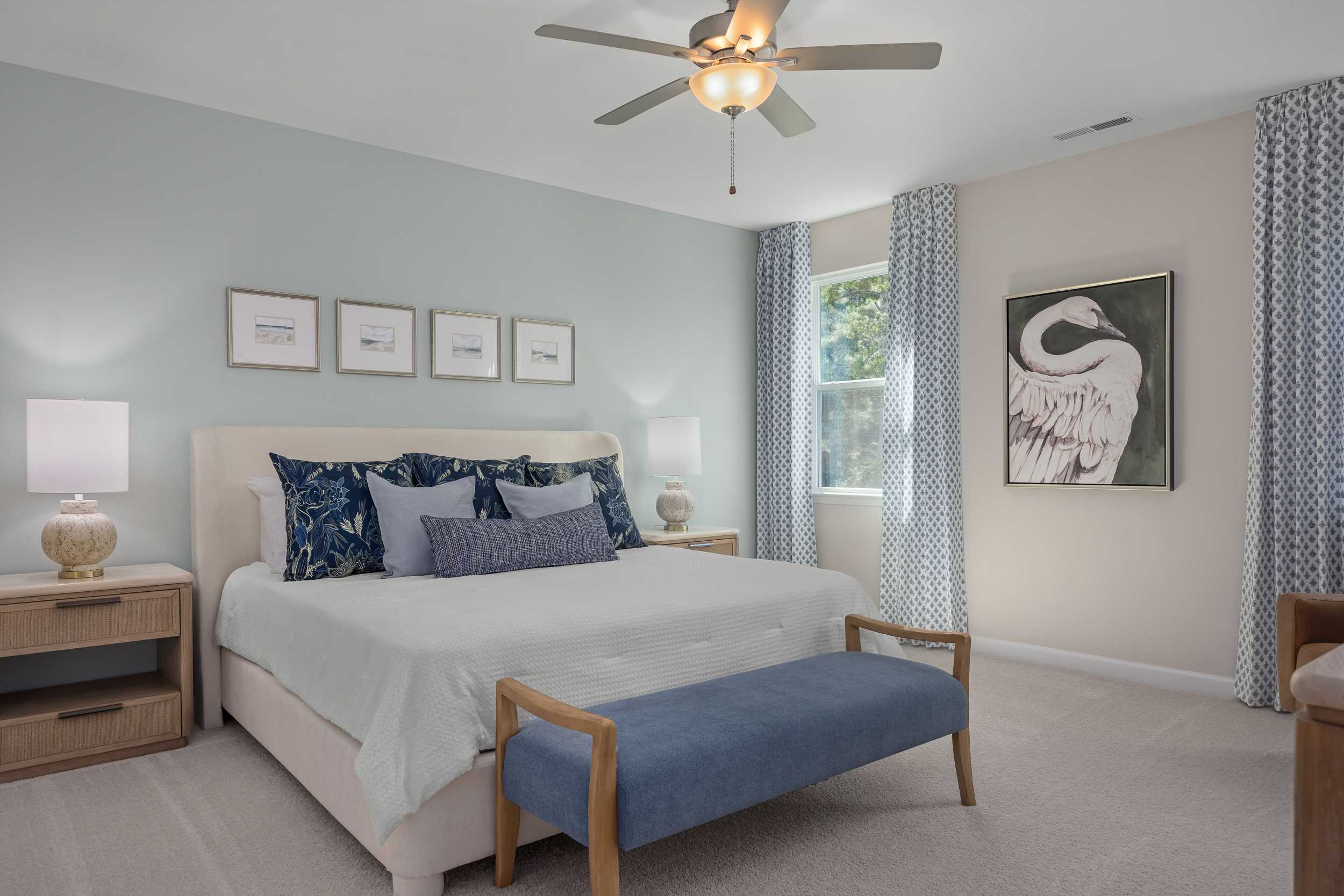Spacious master bedroom in The Hickory II E featuring king bed with blue pillows, ceiling fan, and elegant swan artwork