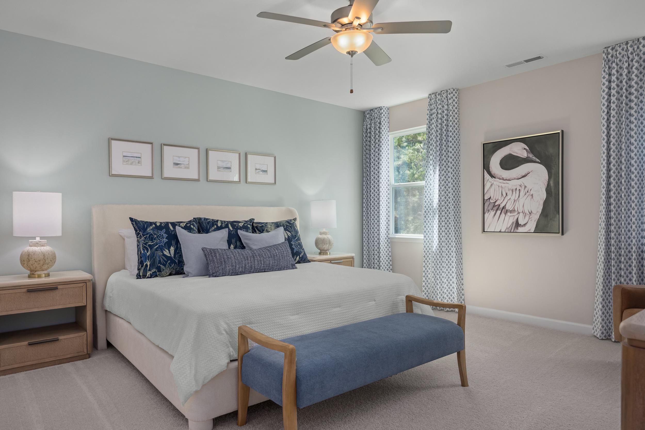 Spacious master bedroom in The Hickory II: king bed with blue pillows, light blue walls, ceiling fan, swan artwork, Holly Springs NC