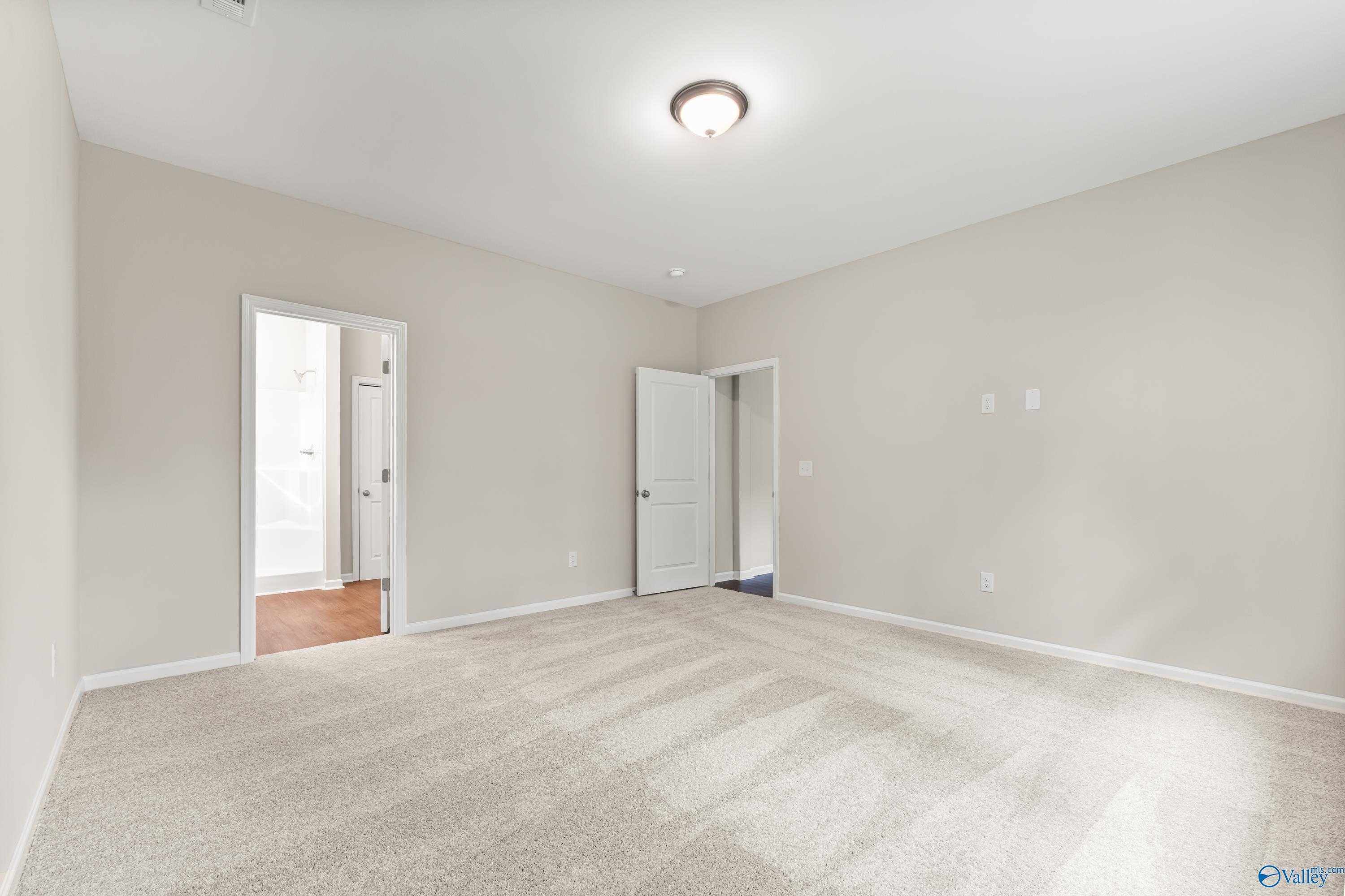 Spacious empty bedroom with beige walls, carpet flooring, and en-suite bathroom door in Davidson Homes The Phoenix, Fayetteville, TN