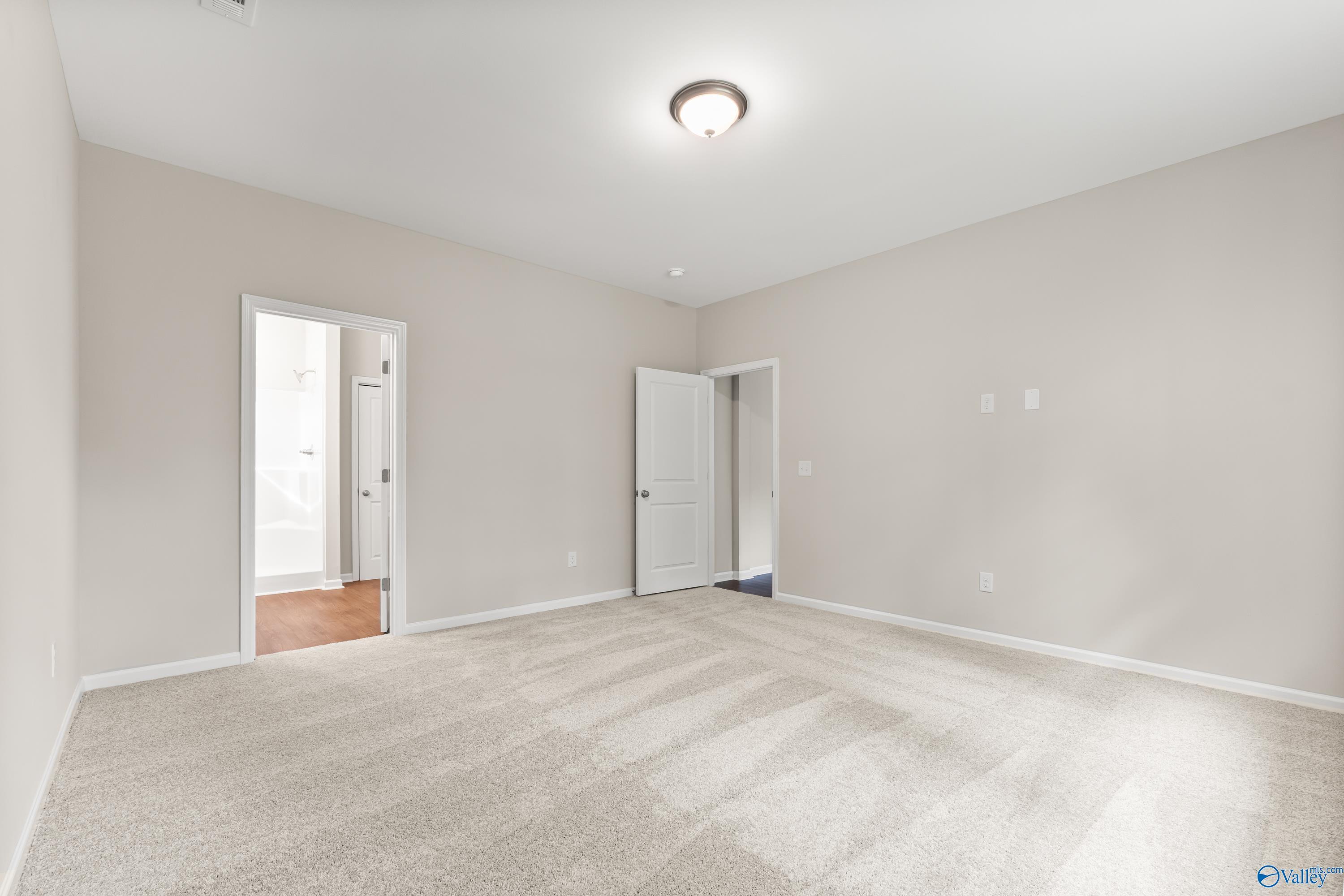 Spacious empty bedroom with neutral beige walls, carpet flooring, and en-suite bathroom door in Davidson Homes The Phoenix, Fayetteville, TN