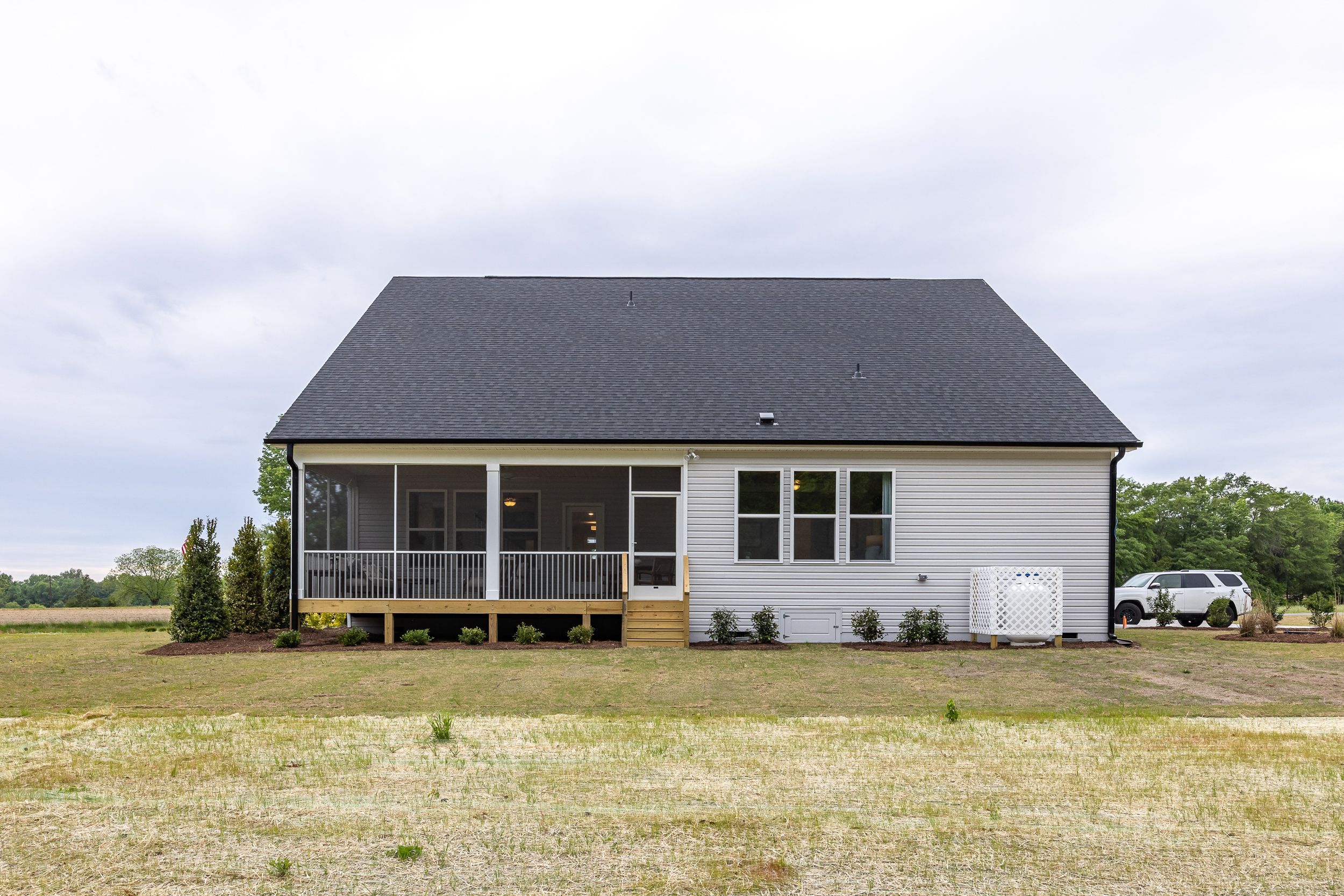Rear elevation of The Magnolia D 1-story home featuring screened porch, vinyl siding, deck, and 2-car garage in Holly Springs NC