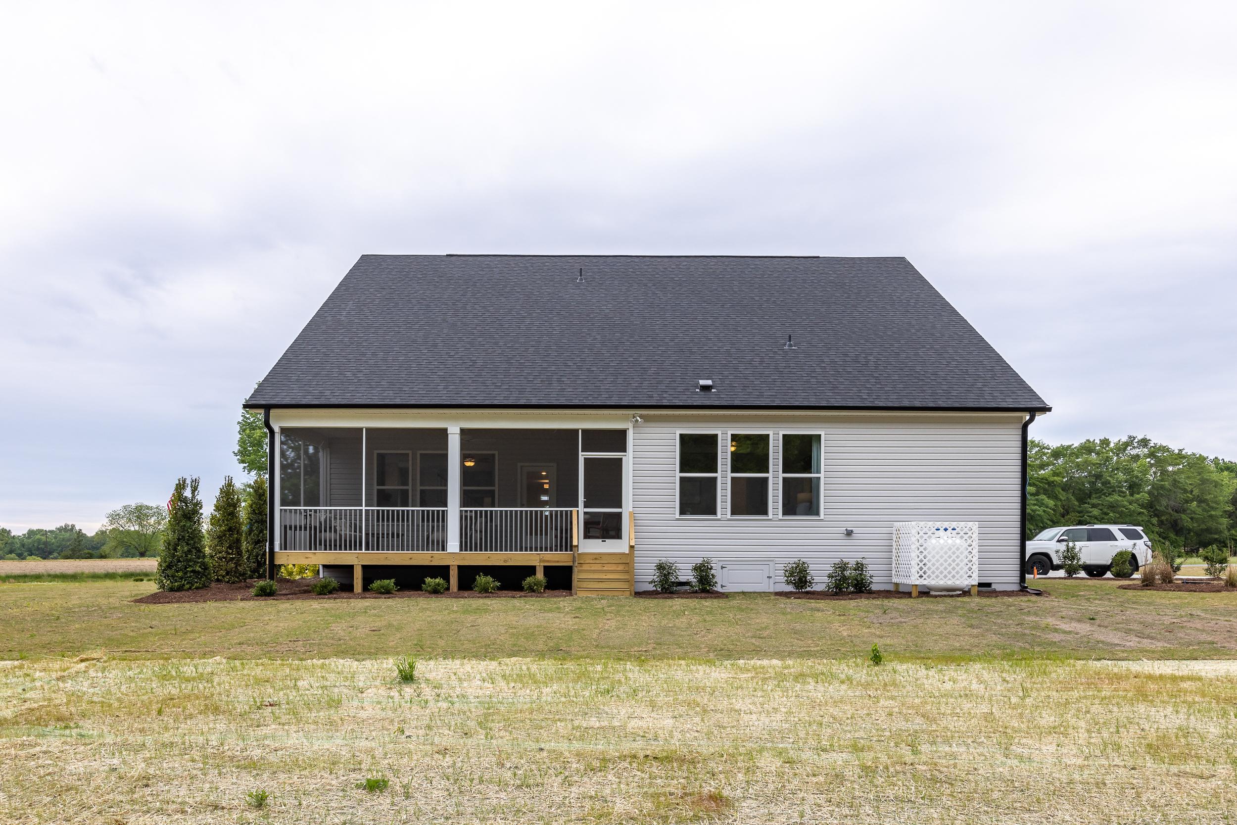 Rear elevation of The Magnolia D 1-story home featuring screened porch, vinyl siding, deck, and 2-car garage in Holly Springs NC