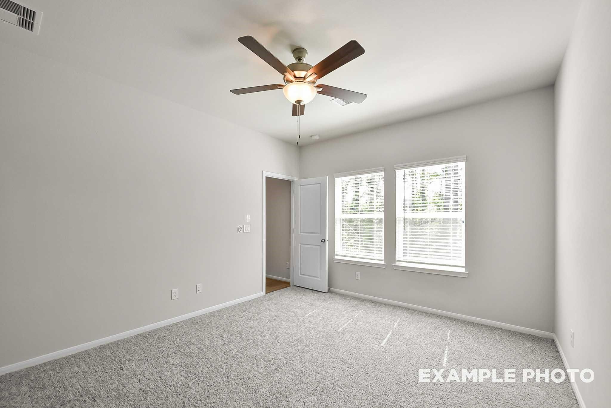 Bright bedroom with plush carpet and ceiling fan in The Blanco F floor plan at Spring Branch Crossing, Conroe, Texas.