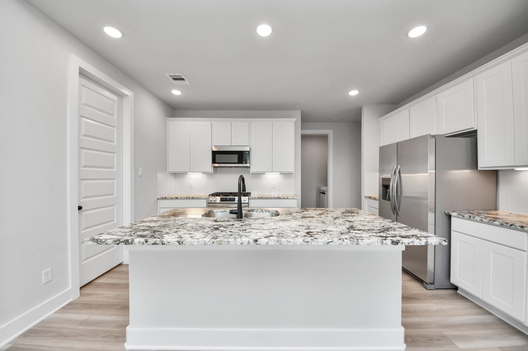 Modern kitchen with granite island and white cabinets in The Laguna C floor plan by Davidson Homes in Sunterra, Katy, TX.