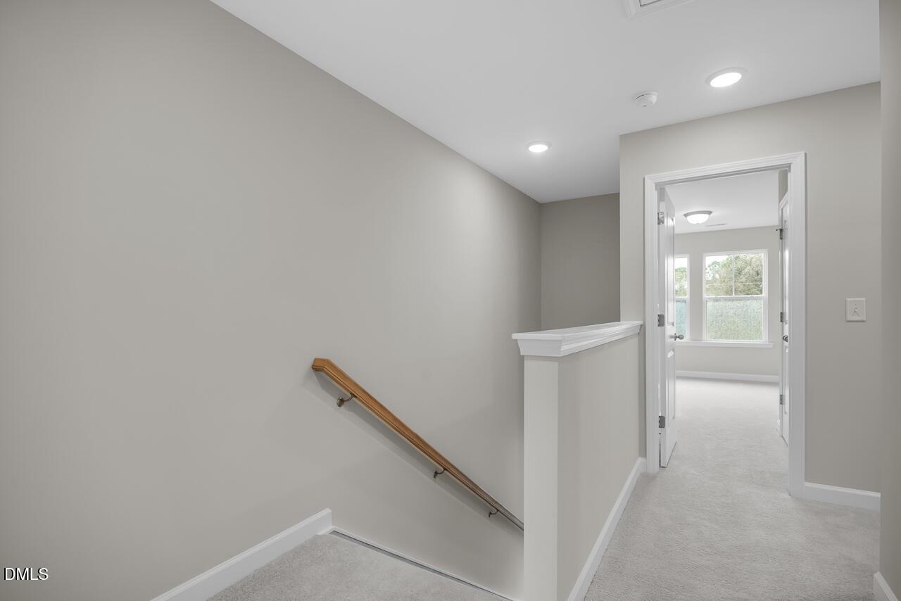 Elegant light gray hallway with wooden staircase railing, white trim, carpeted floors, and open doors to sunlit rooms in Davidson Homes The Avery, Knightdale, NC