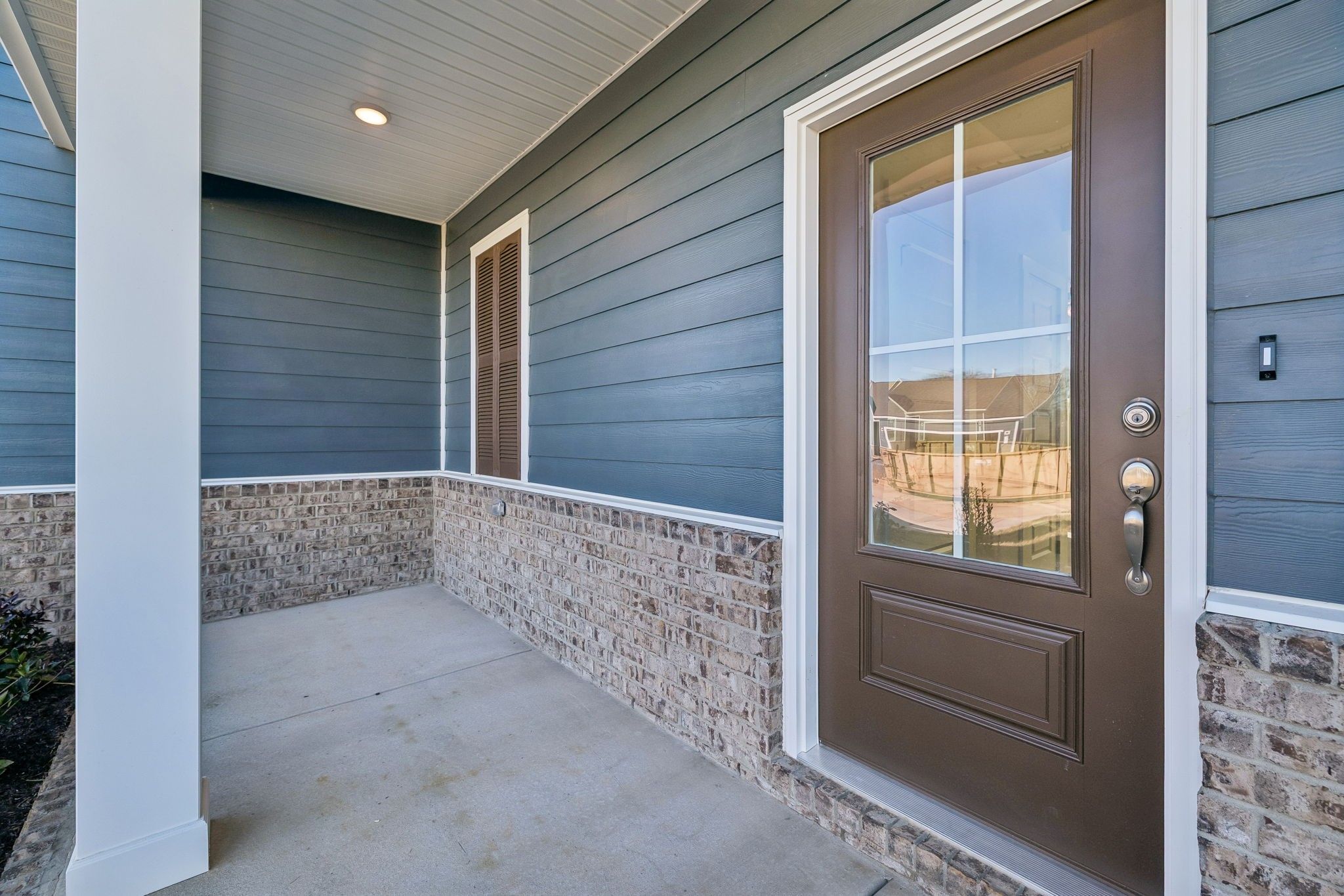 Welcoming covered front porch with white columns, blue siding, stone base, and glass-paneled mahogany door in Sage Farms, White House, Tennessee