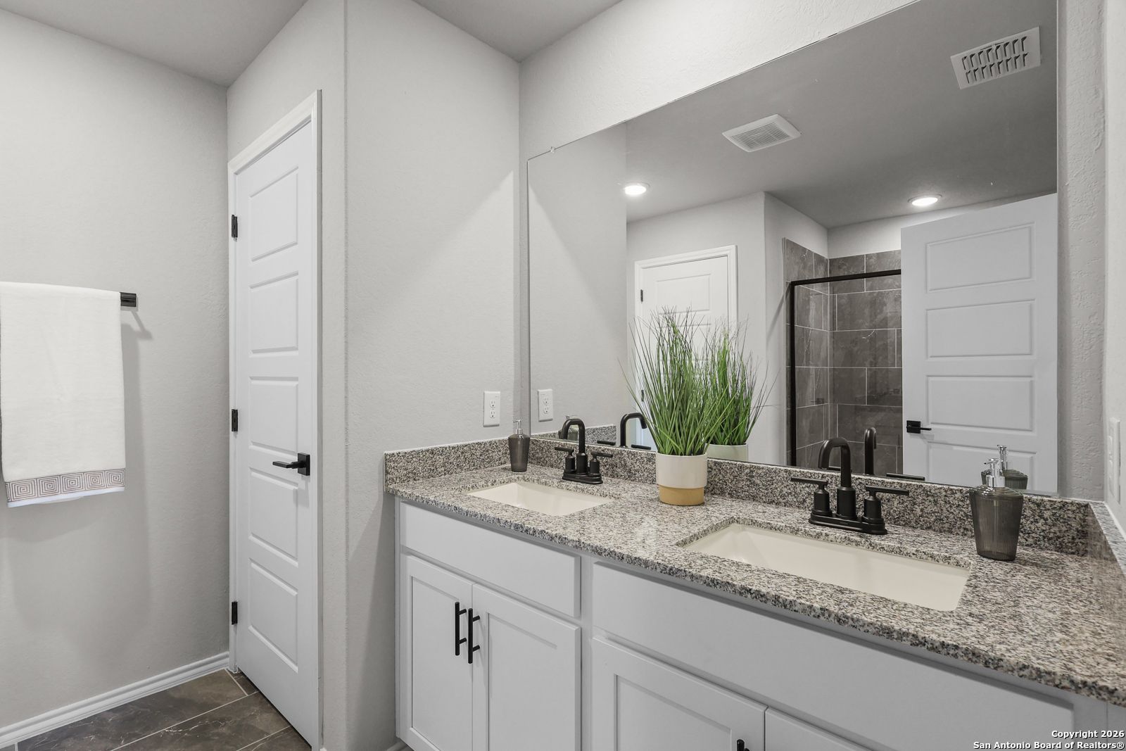 Modern master bathroom featuring double granite vanity, white cabinets, large mirror, and glass shower in Davidson Homes The Murray K, San Antonio