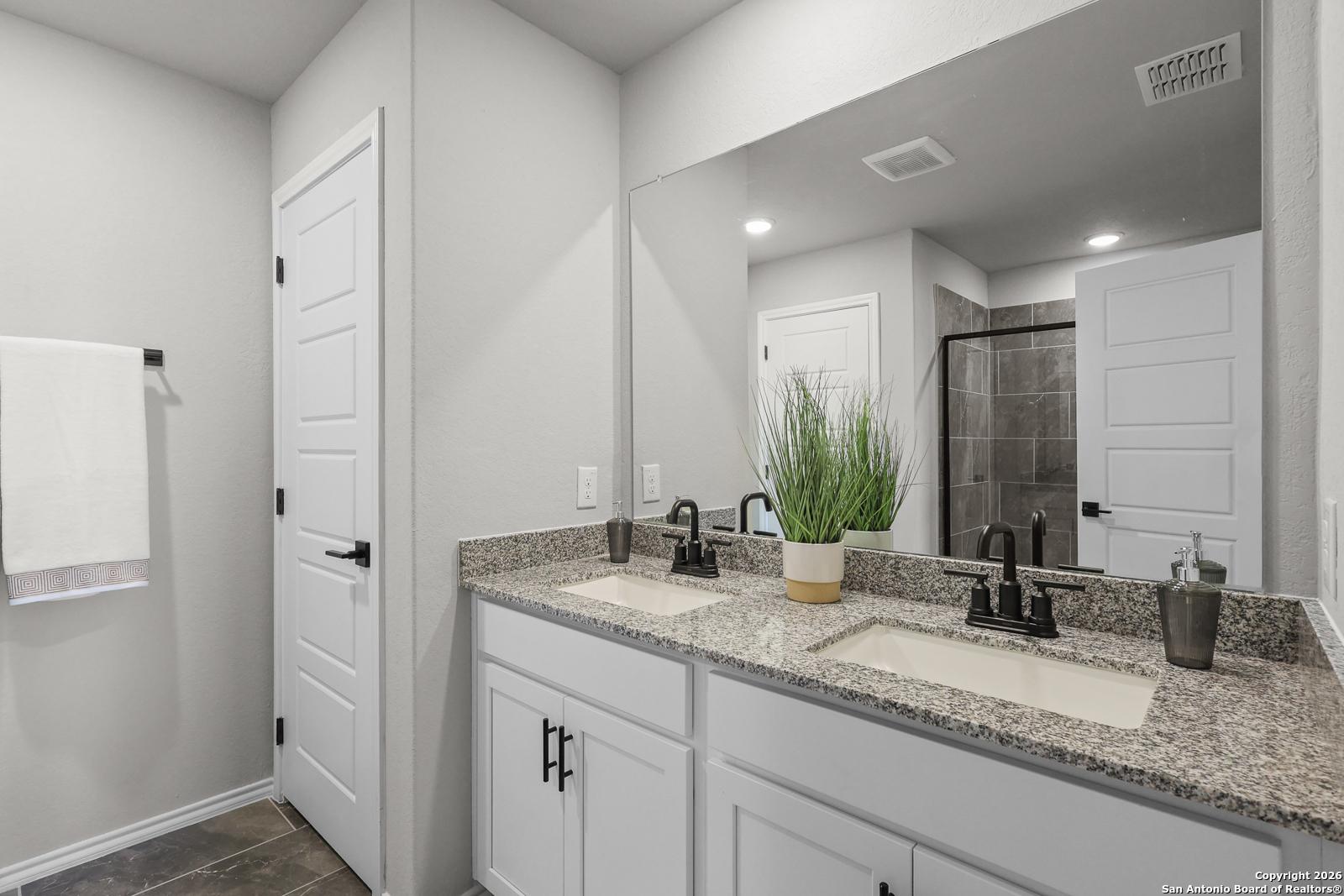 Modern master bathroom featuring double granite vanity, white cabinets, large mirror, and glass shower in Davidson Homes The Murray K, San Antonio