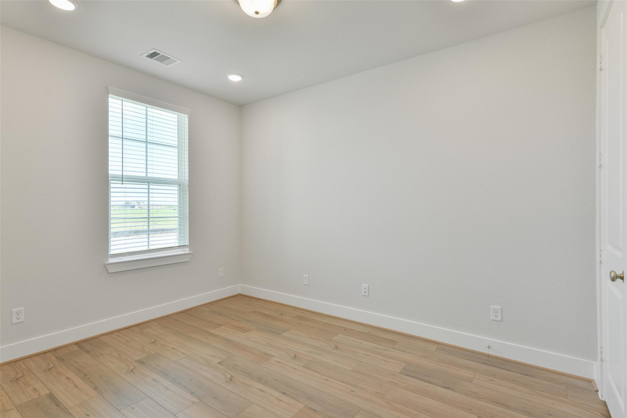 Bright empty bedroom featuring hardwood floors, large window with blinds, and neutral walls in Davidson Homes The Edward A, Lago Mar