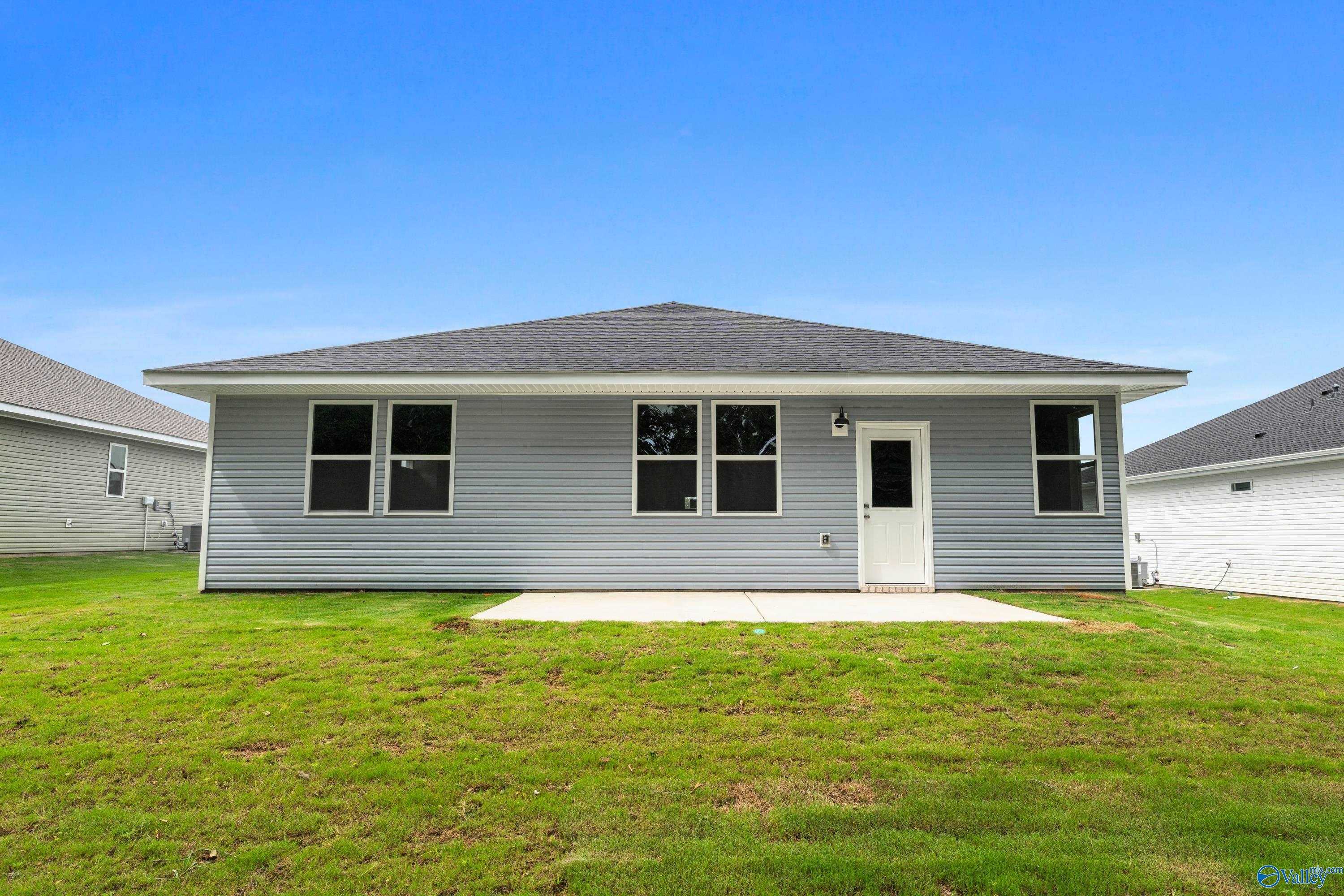 Rear view of single-story 3-bedroom Davidson Homes The Phoenix: gray siding, three windows, back door, concrete patio, lush green yard in Bailey Park, Fayetteville, TN