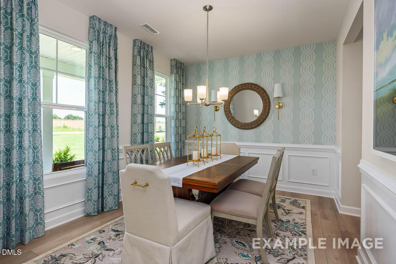 Elegant dining room with wooden table, blue patterned wallpaper, chandelier, and large windows in The Willow B 4-bedroom home, Wake Forest, NC