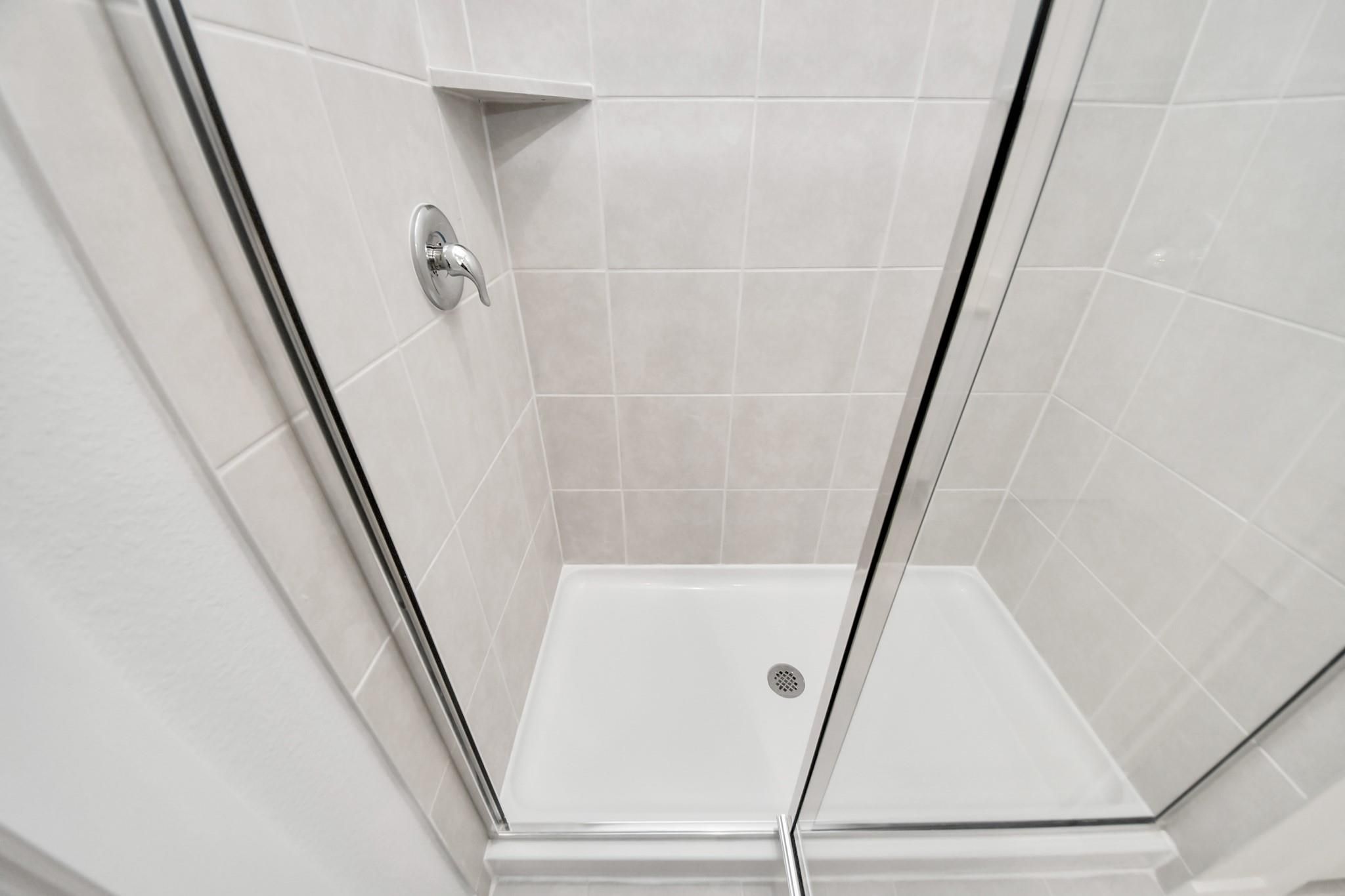 Tiled walk-in shower with glass enclosure in The Blanco E floor plan at Caney Creek Place, Conroe, Texas.
