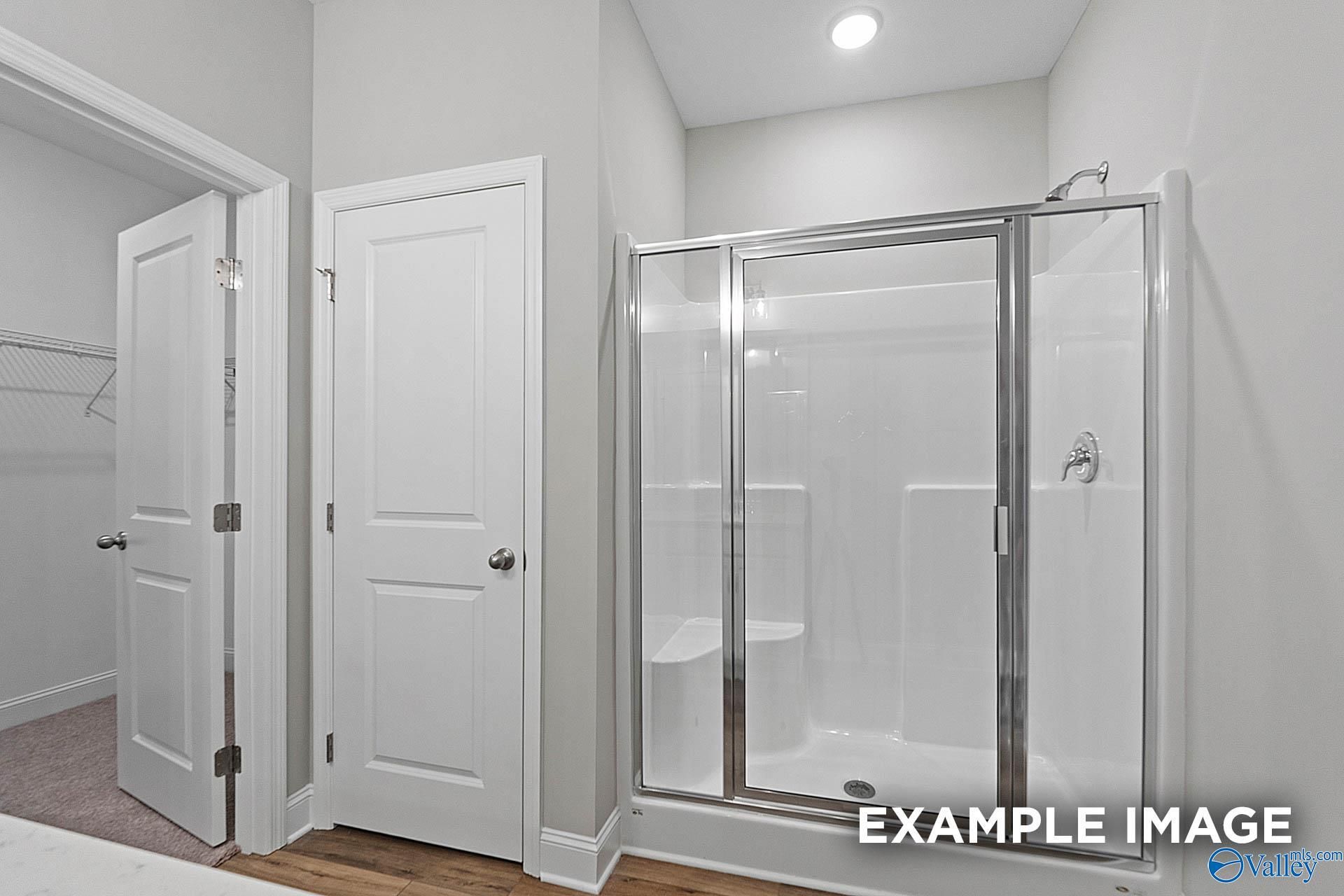Modern master bathroom with glass shower enclosure, bench seat, and walk-in closet in Davidson Homes The Franklin E, Hazel Green, Alabama