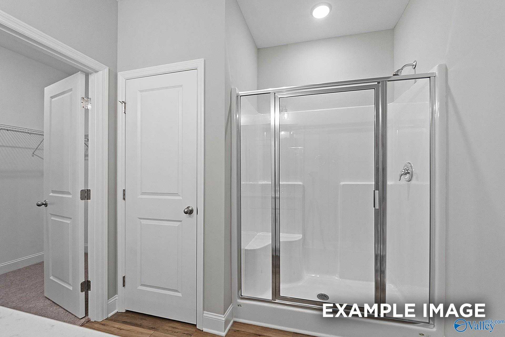 Modern master bathroom with glass shower enclosure, bench seat, and walk-in closet in Davidson Homes The Franklin E, Hazel Green, Alabama