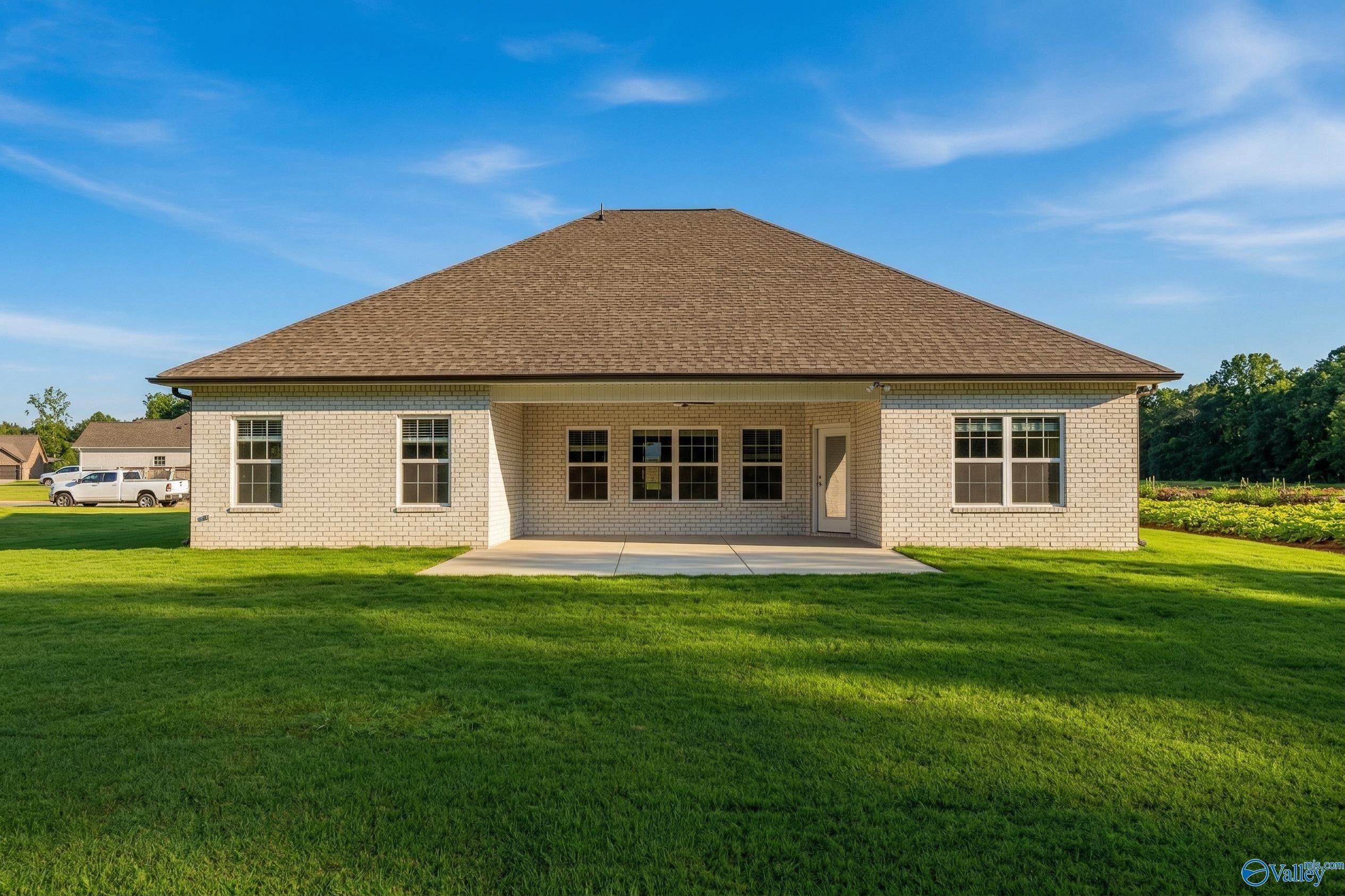 Rear view of The Rockford 1.5-story brick home with covered patio, large windows, and green lawn in Cain Park, Hartselle, Alabama