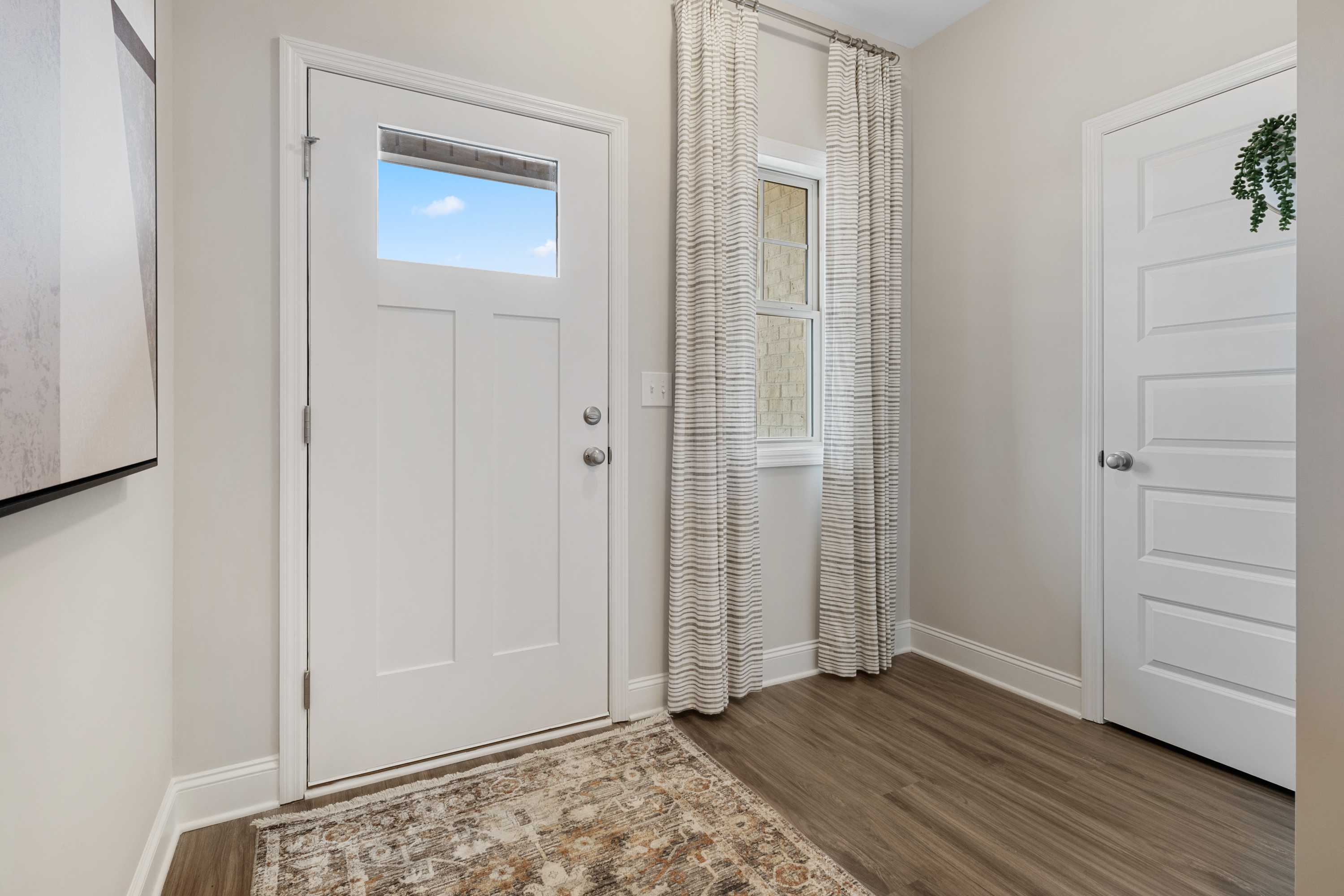 Spacious entryway at The Retreat at Cain Park in Hartselle Alabama with white doors, striped curtains, hardwood floors