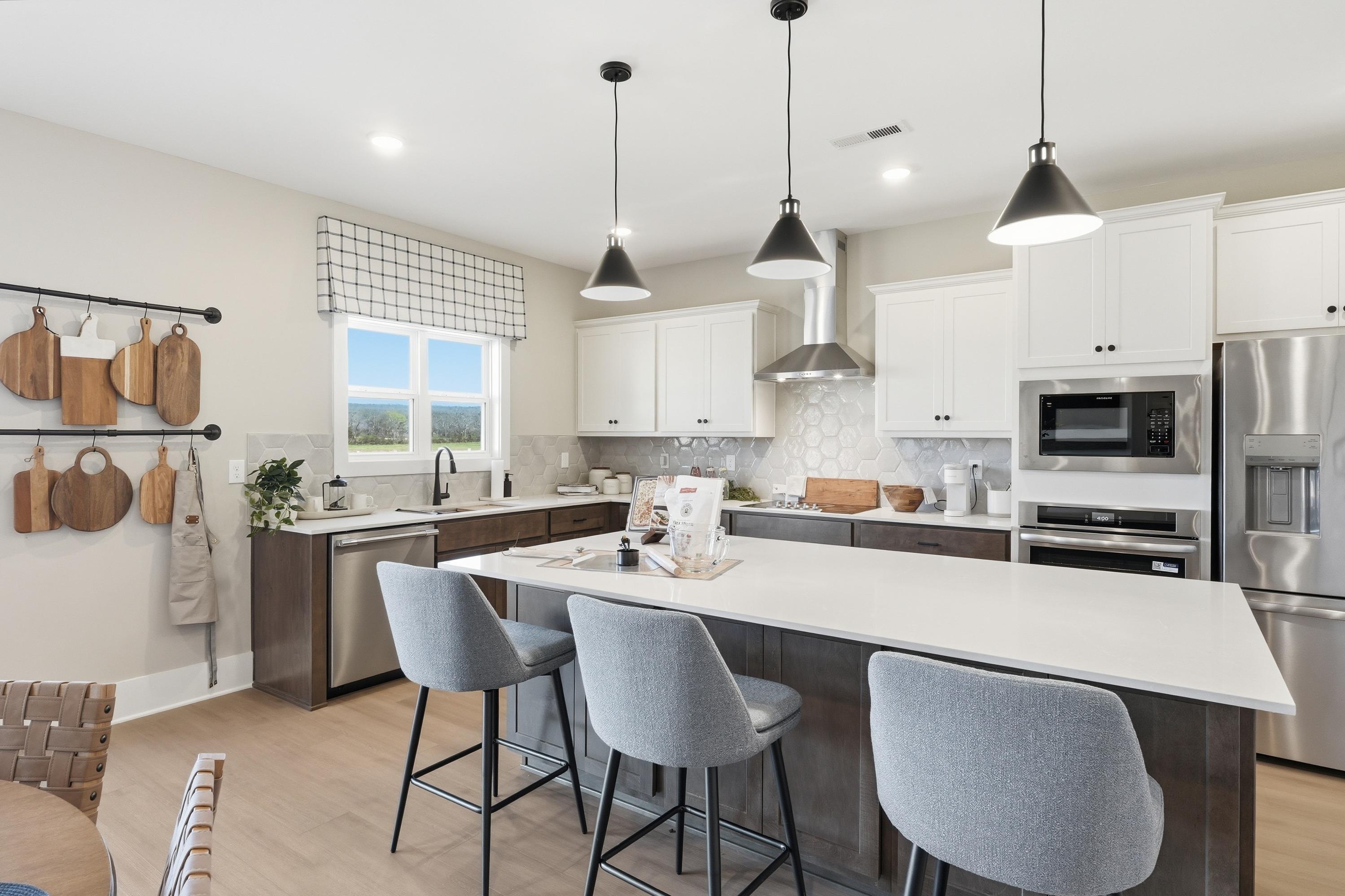 Modern kitchen in Berry Cove home, New Market Alabama with white shaker cabinets, large island, stainless steel appliances, and pendant lights