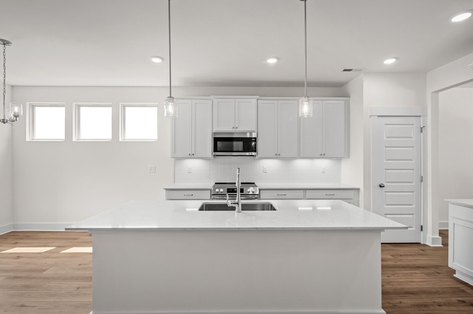 Modern kitchen with white cabinets, quartz island, and stainless steel appliances in The Ash A floor plan, Gallatin, TN.