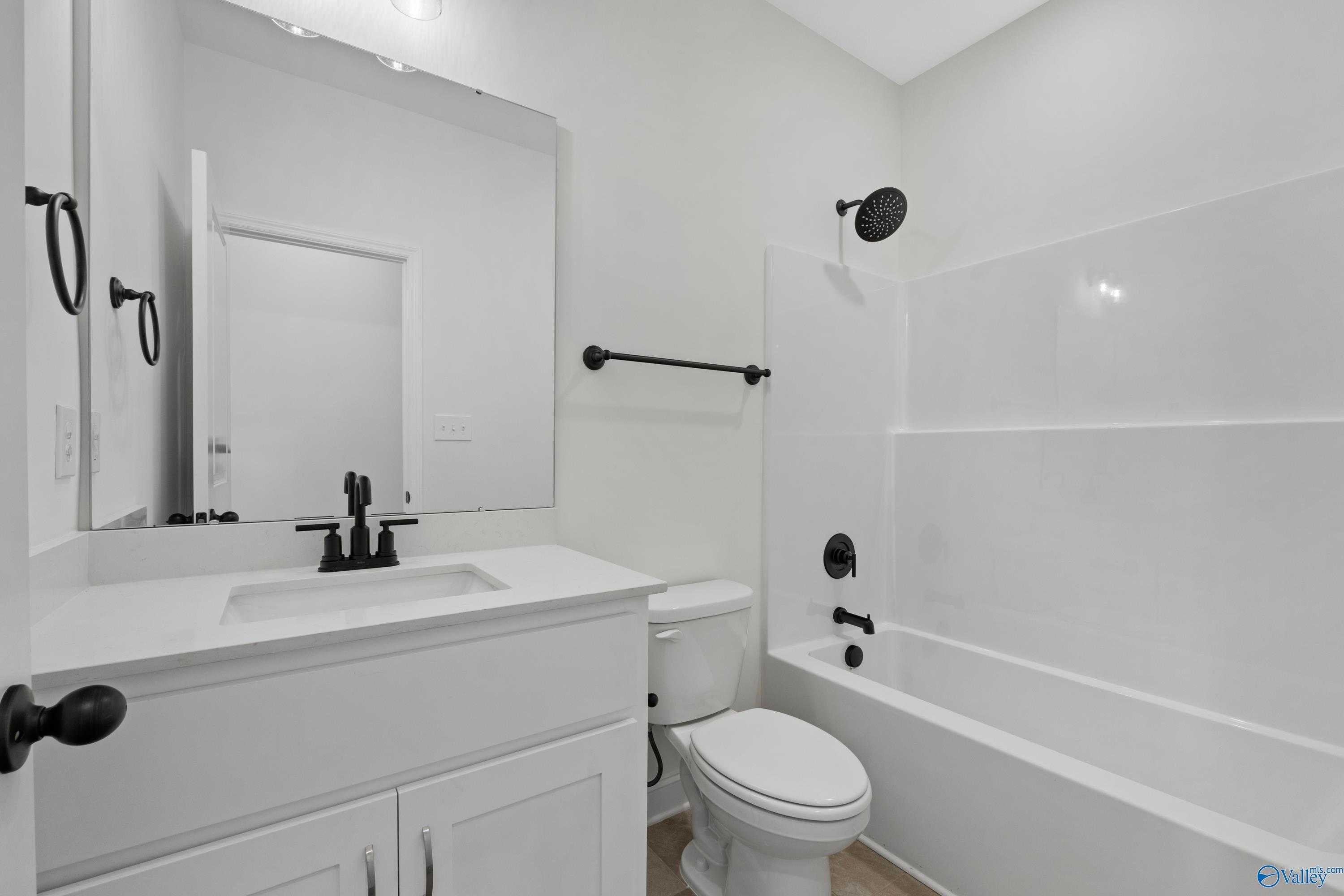 Modern white bathroom with black fixtures, single vanity sink, large mirror, toilet, and tub-shower combo in Davidson Homes The Rockford B, Toney Alabama