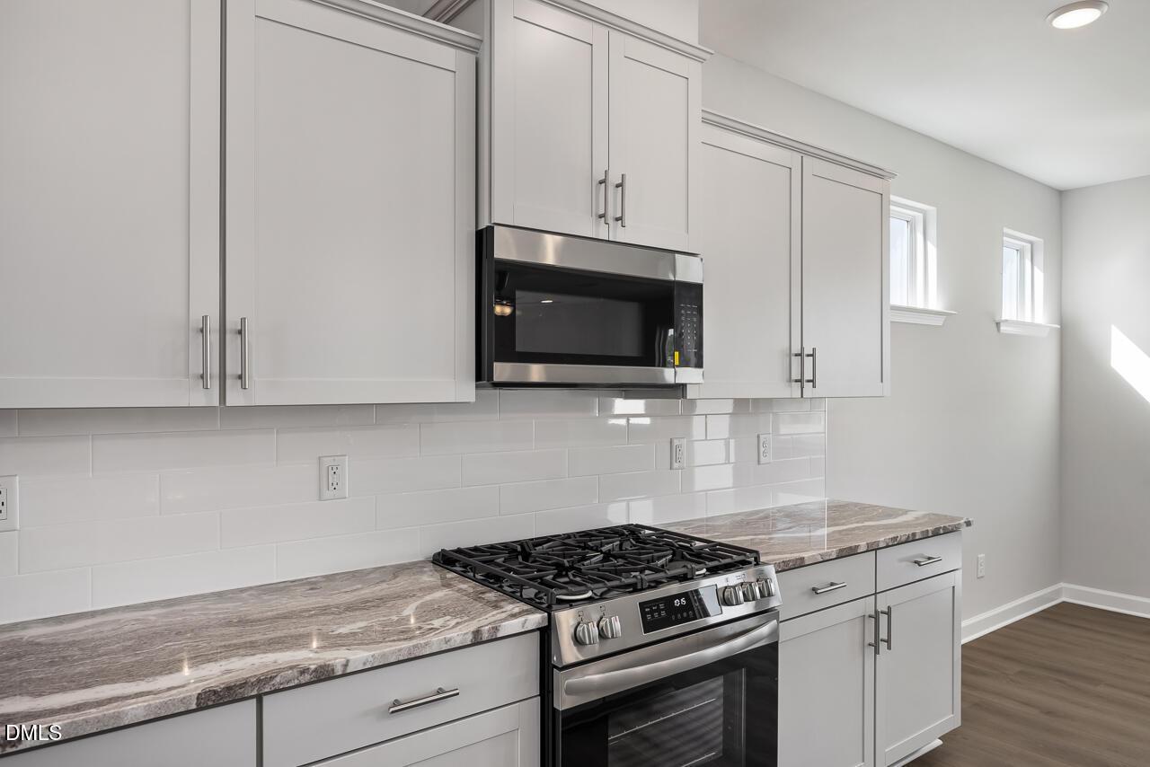 Modern white shaker kitchen with subway tile backsplash, quartz countertops, stainless gas range in The Willow G by Davidson Homes, Angier, NC