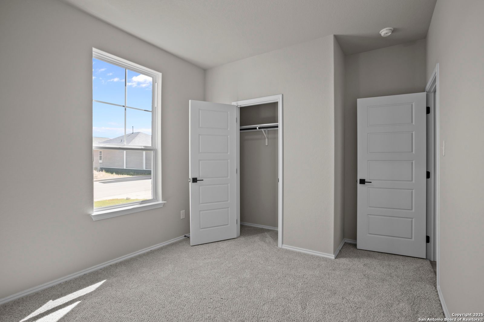 Bright secondary bedroom with dual open closets, gray walls, carpet floor, and large window in Davidson Homes The Asheville H, Converse, Texas