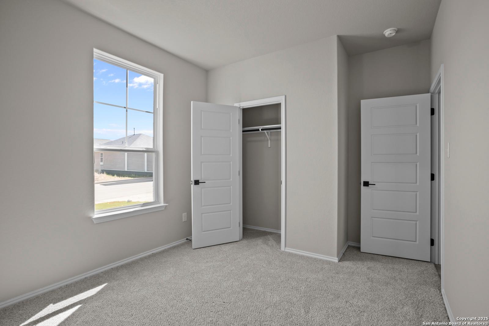 Bright secondary bedroom with dual open closets, gray walls, carpet floor, and large window in Davidson Homes The Asheville H, Converse, Texas