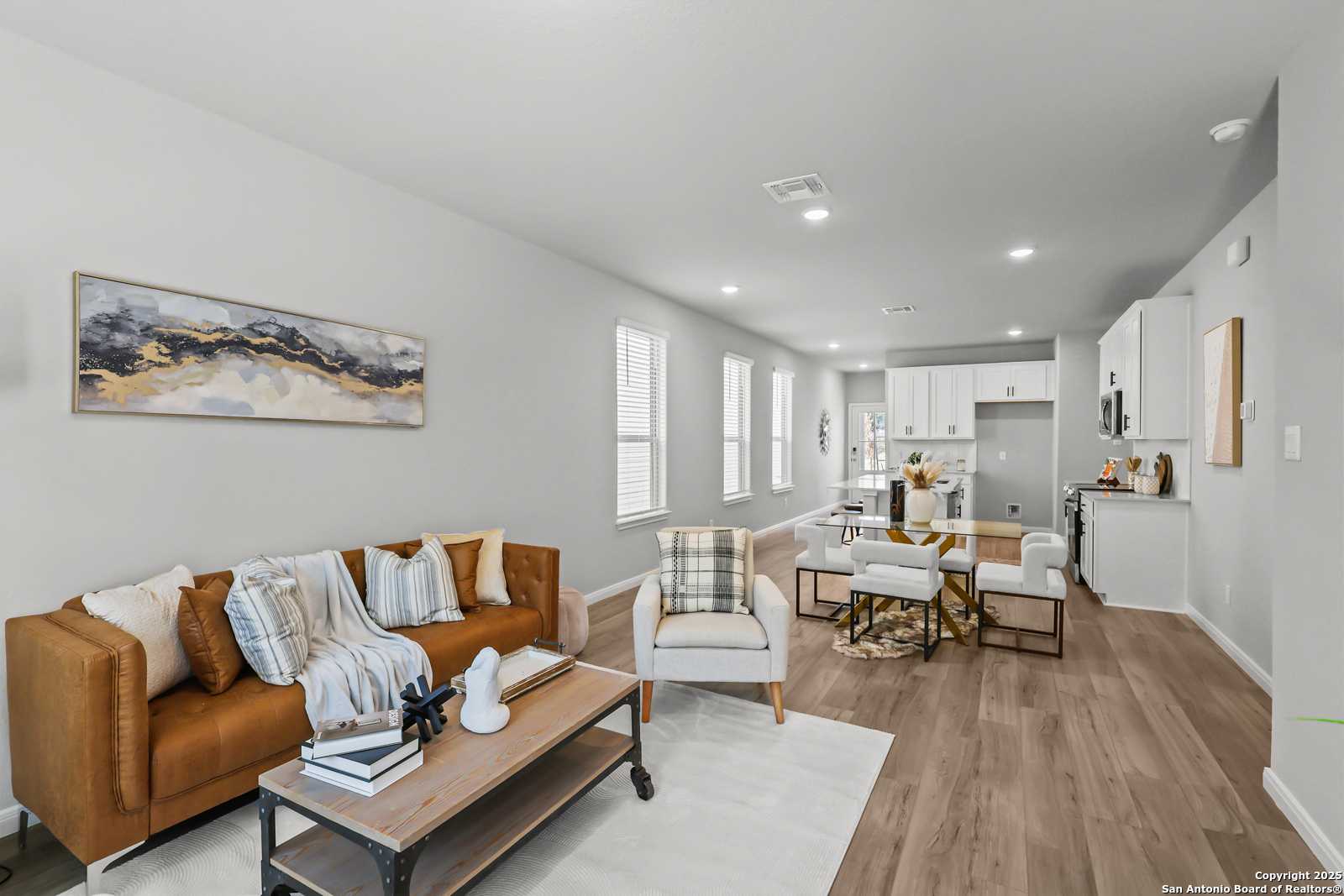 Open-concept living room with tan leather sofa, wood coffee table, and adjacent dining area in Davidson Homes The Gillian C, San Antonio
