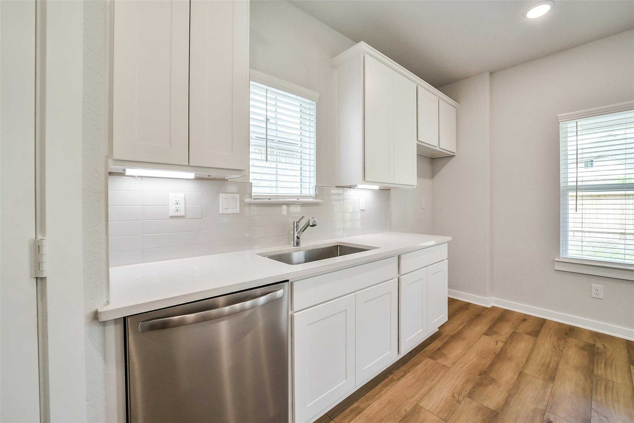 Modern white kitchen featuring shaker cabinets, quartz counters, stainless dishwasher in Davidson Homes The Trinity F, Magnolia, Texas
