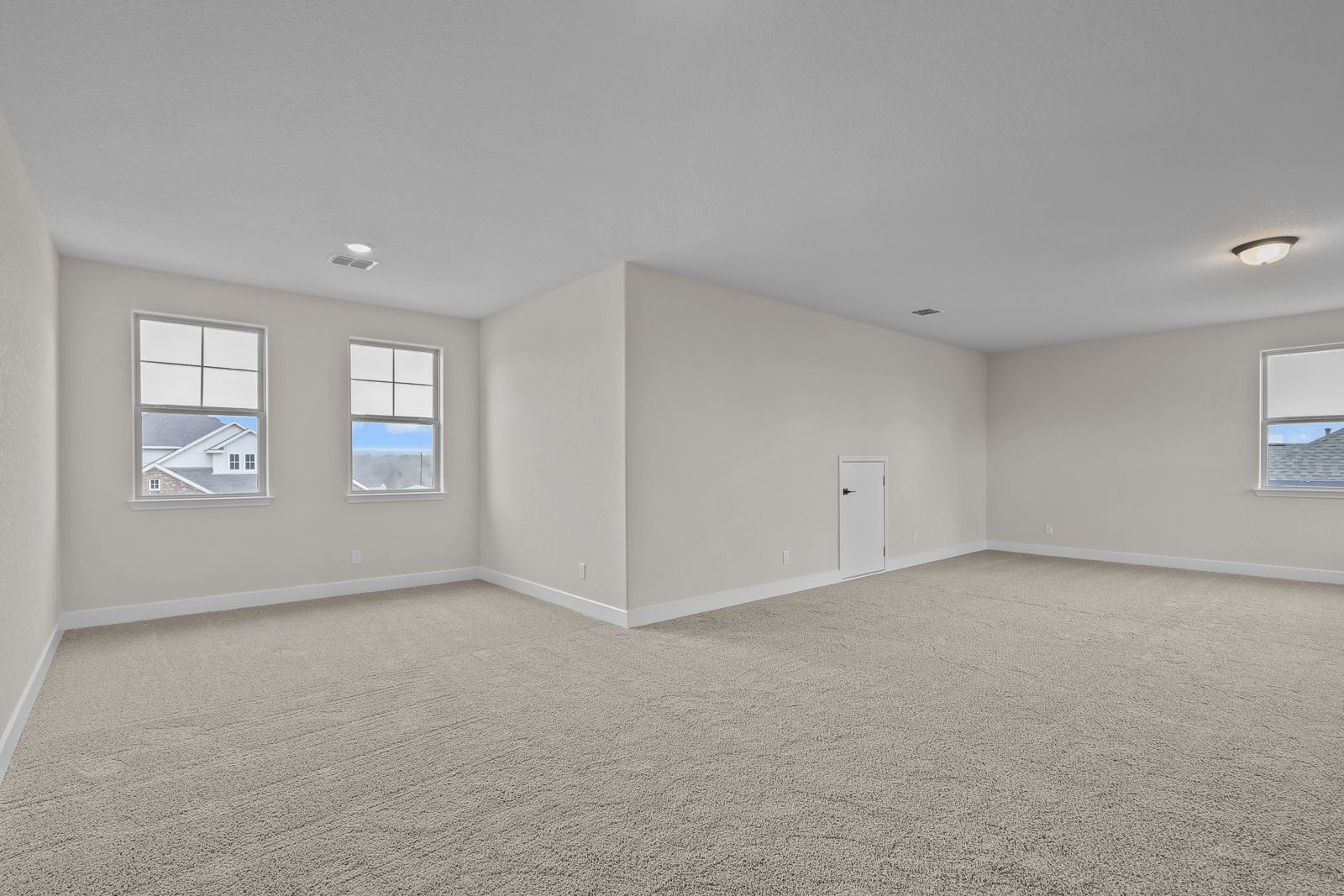 Spacious carpeted loft in The Belmont home design featuring neutral walls, ample natural light, and attic access door.