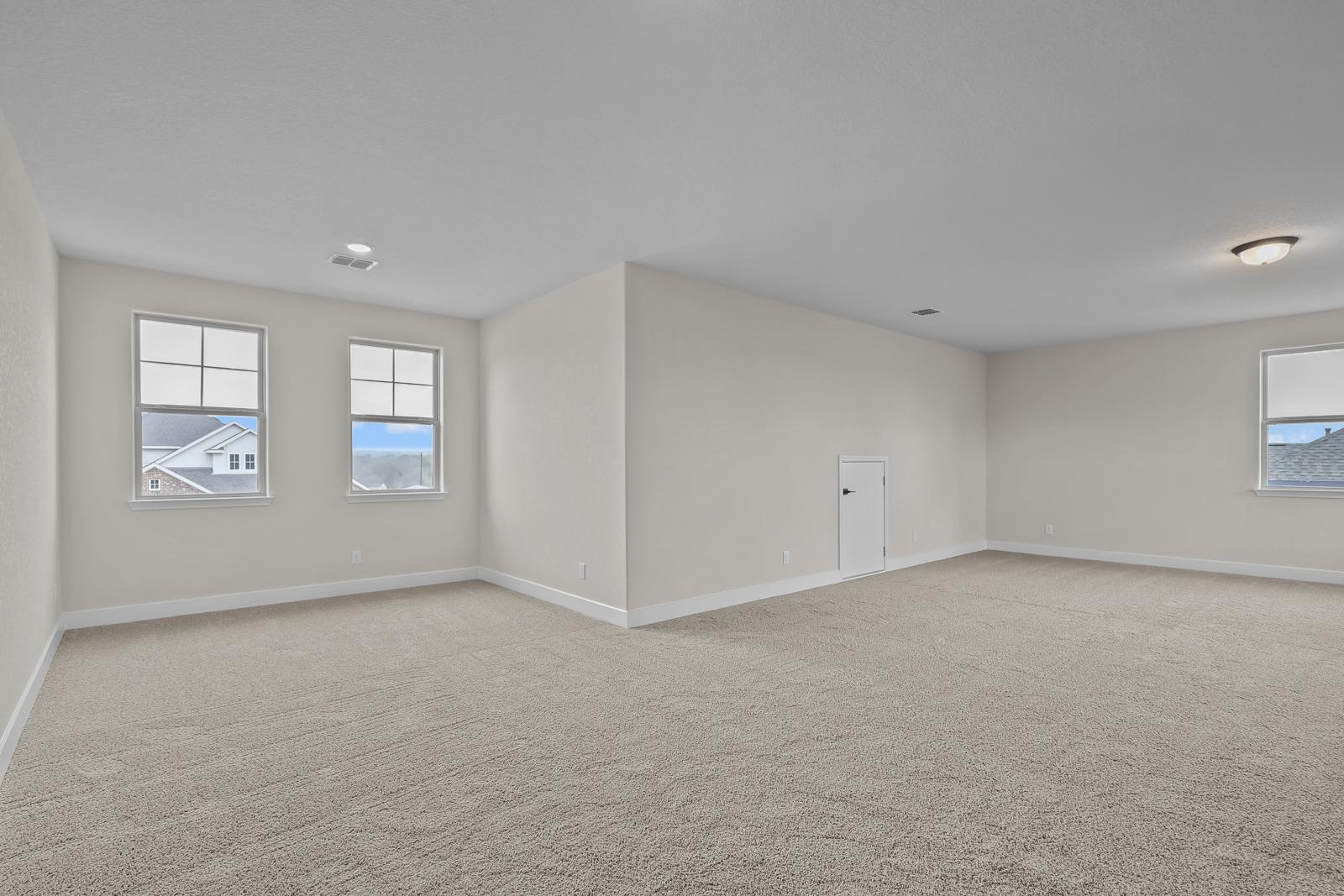 Spacious carpeted loft in The Belmont home design featuring neutral walls, ample natural light, and attic access door.